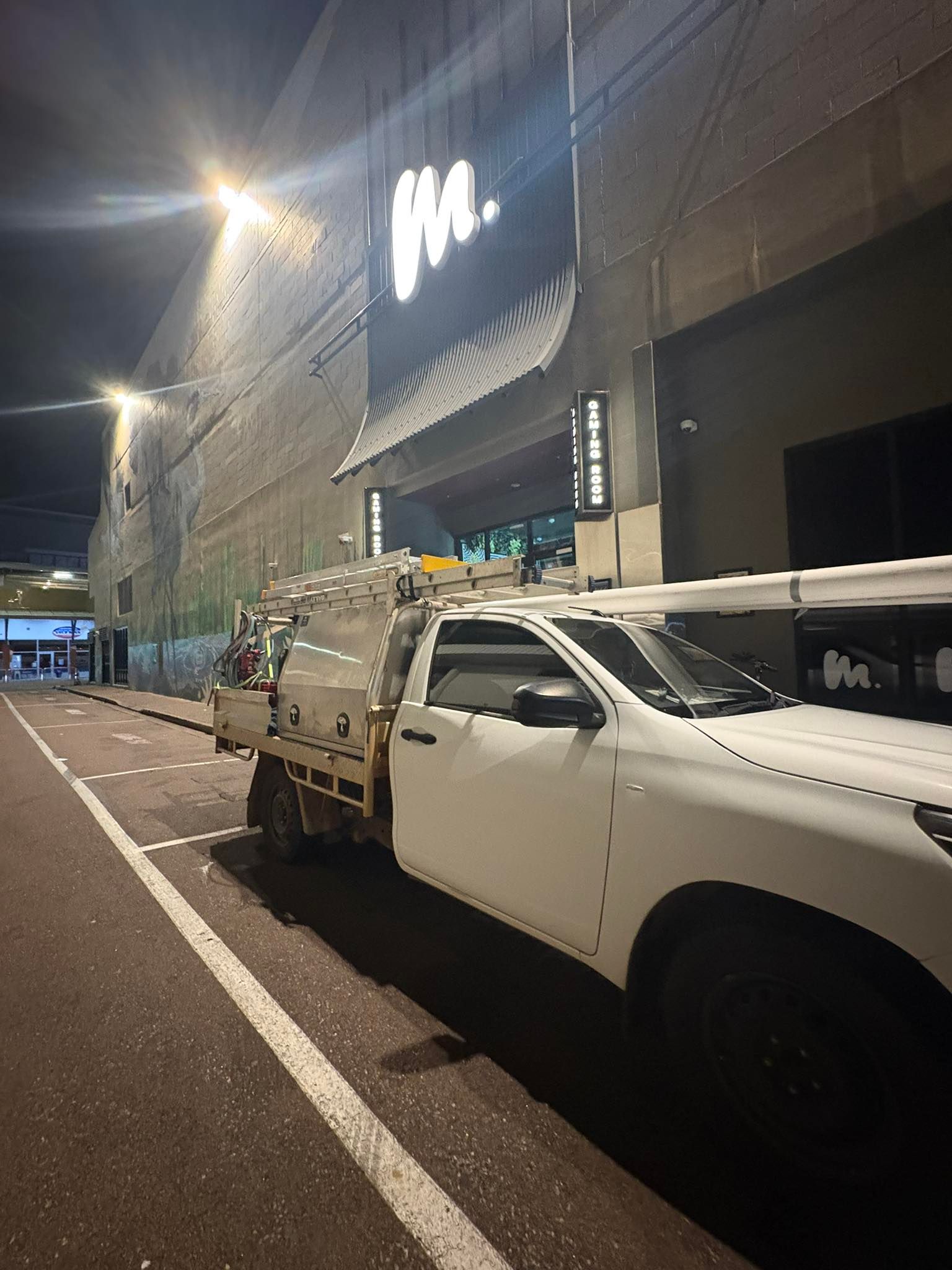 A white truck is parked on the side of the road in front of a building at night.