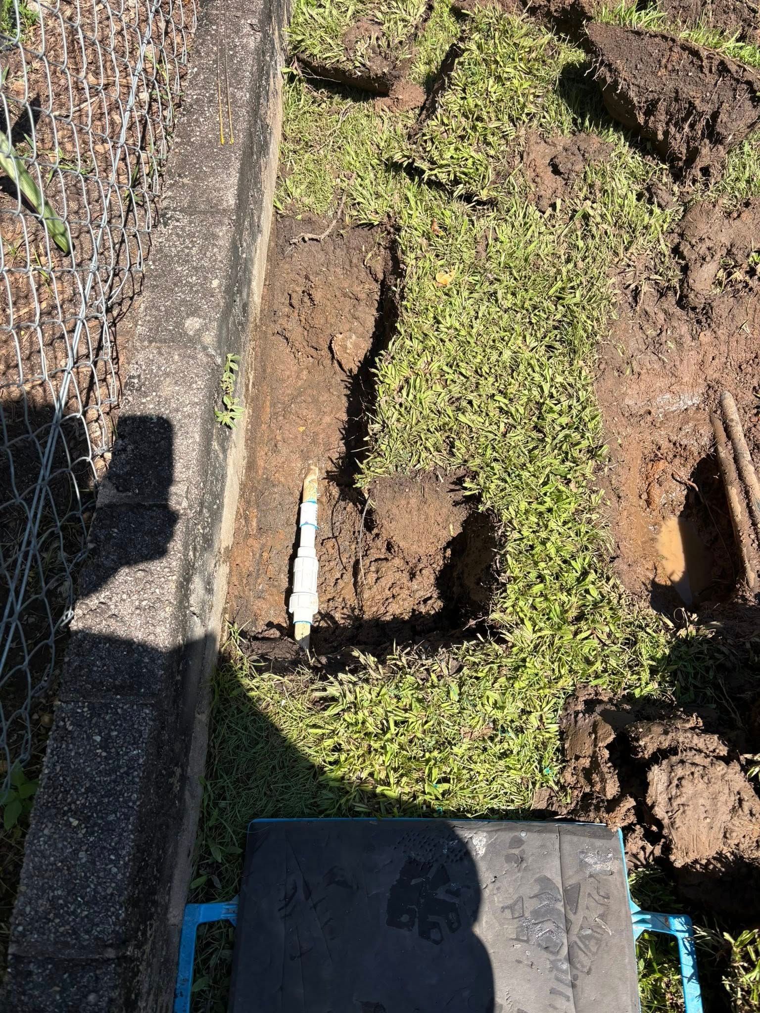 A person is digging a hole in the ground next to a fence.