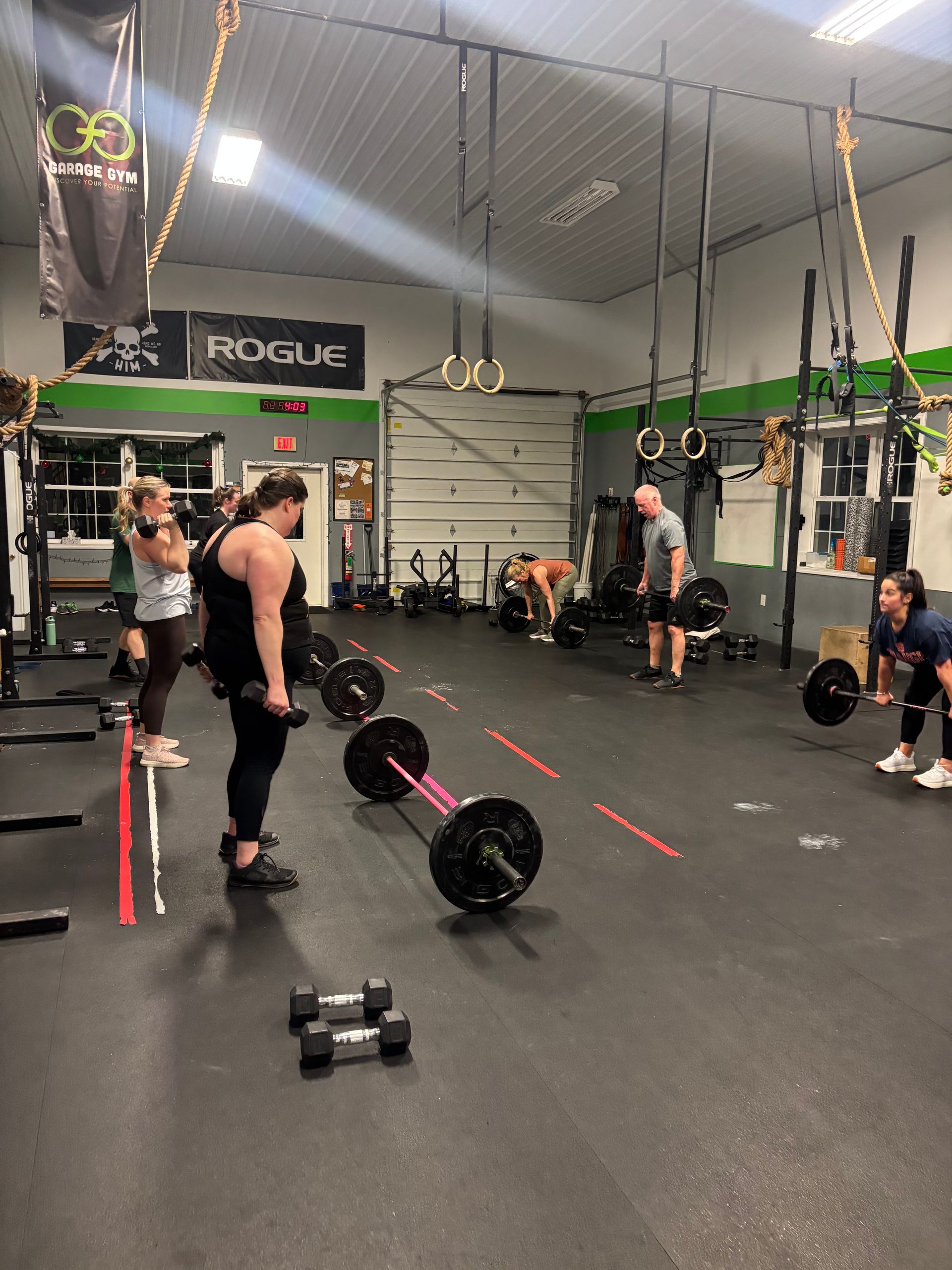 People lifting barbells in a CrossFit gym with hanging rings and green accents