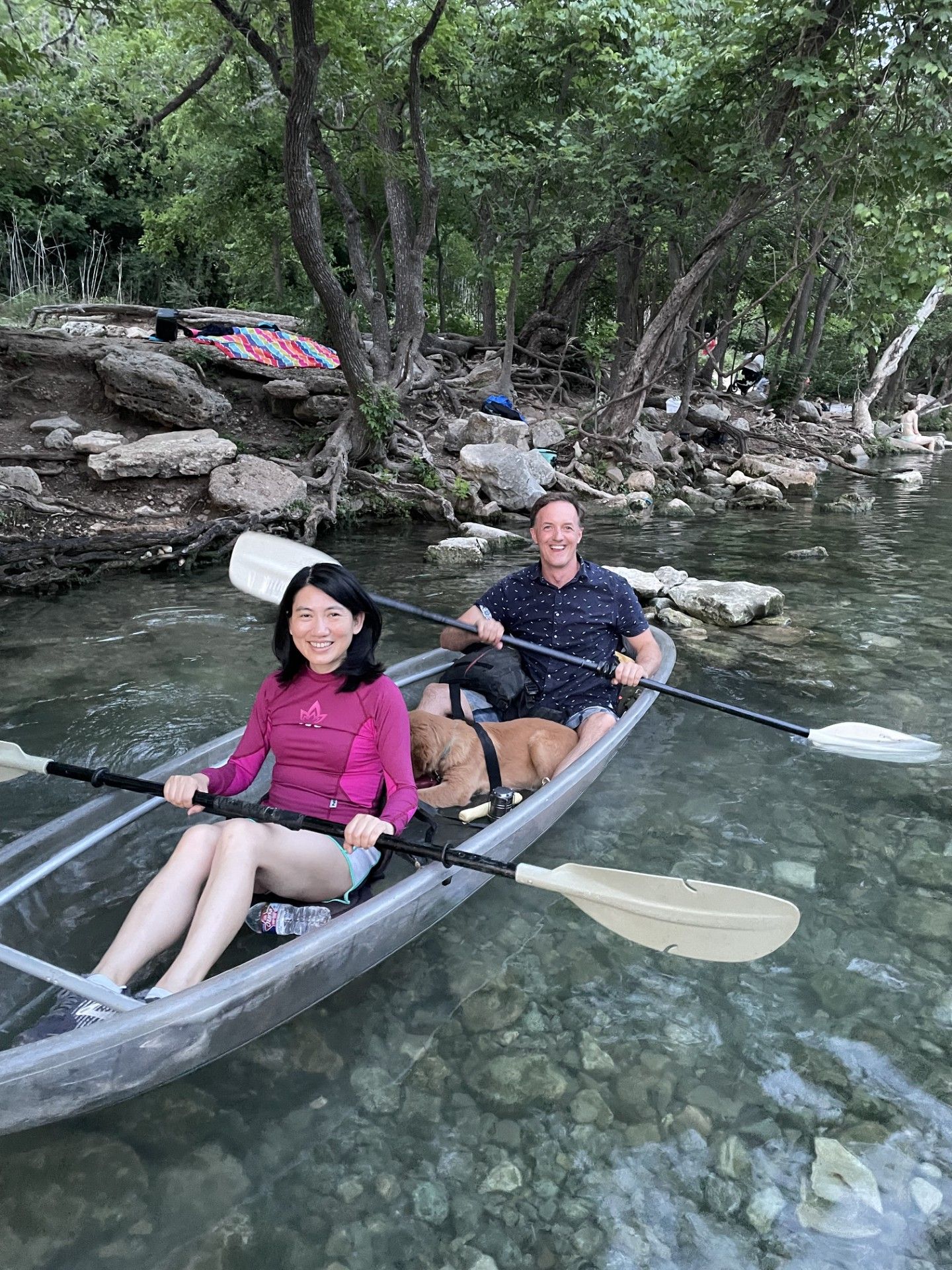 Two people kayaking on clear water, a dog sits between them.