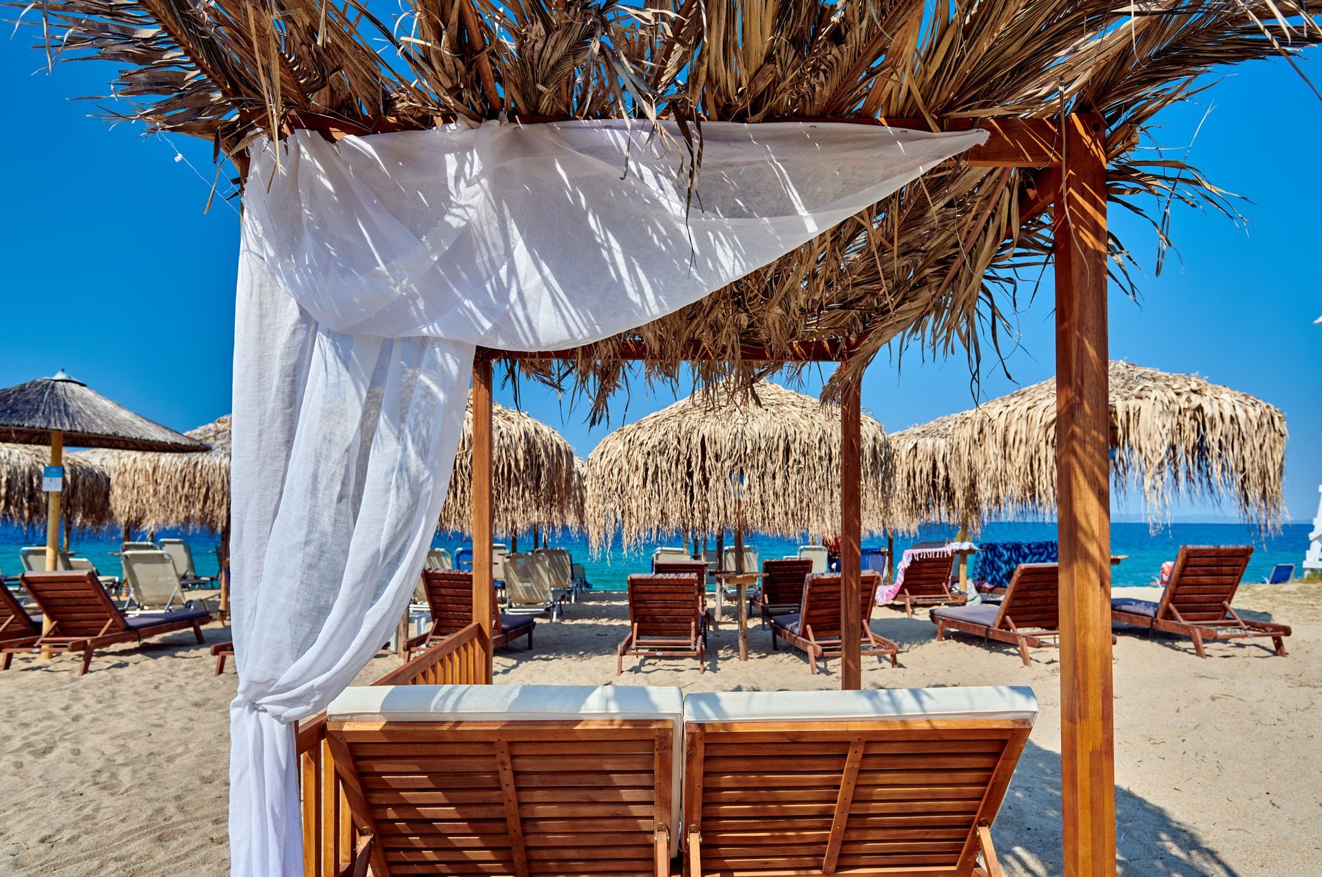 Beach cabana with white curtains and sun loungers facing the ocean.