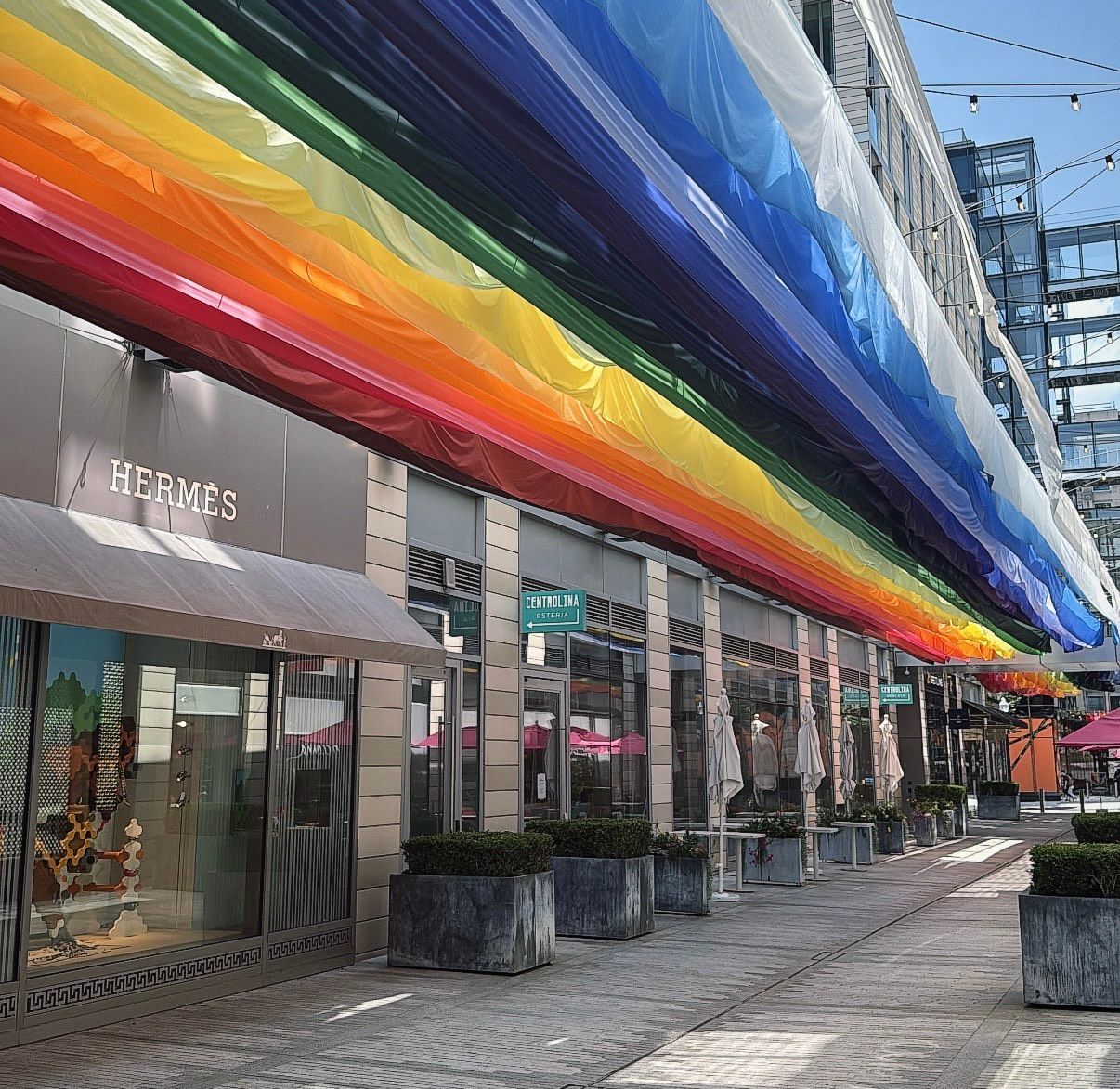 Shops with rainbow-colored canopy, planters, and paved walkway.