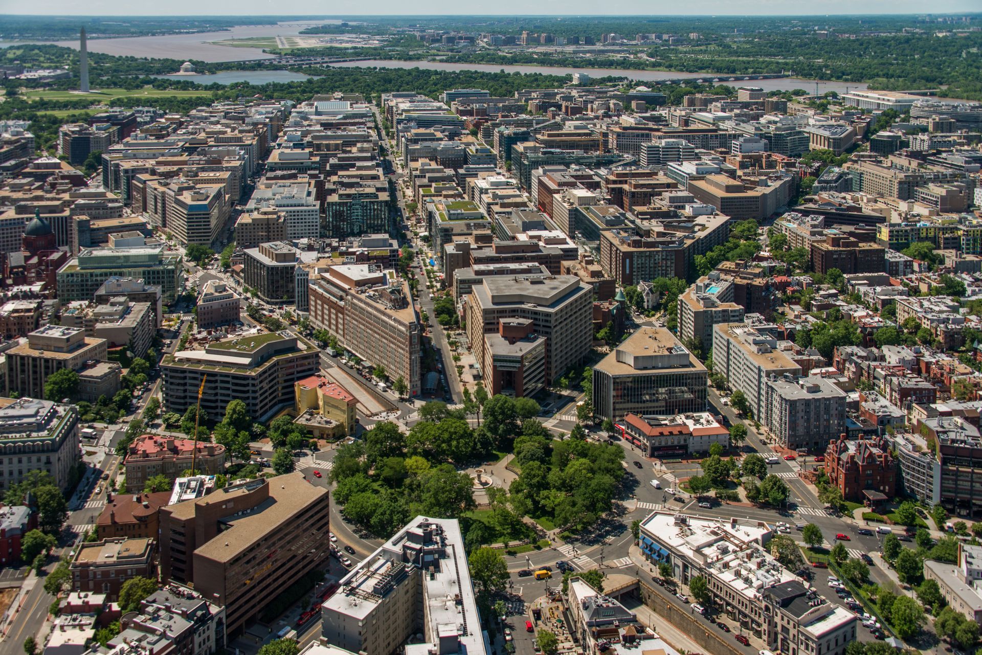 Aerial view of Washington, D.C., with buildings, streets, trees, and the National Mall visible in the background.