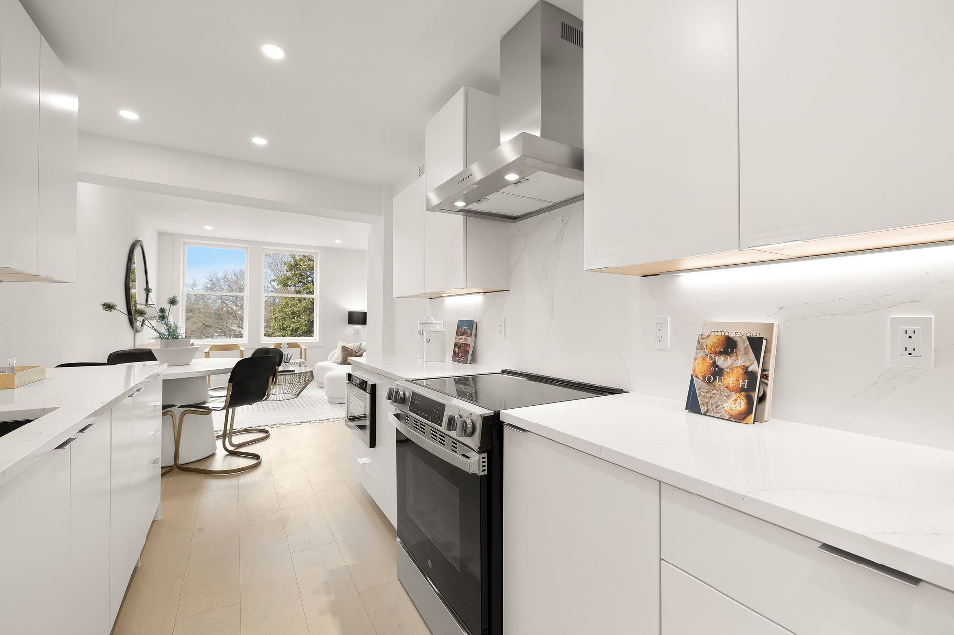 Bright white kitchen with stainless steel appliances, open to a dining and living space with a window view.