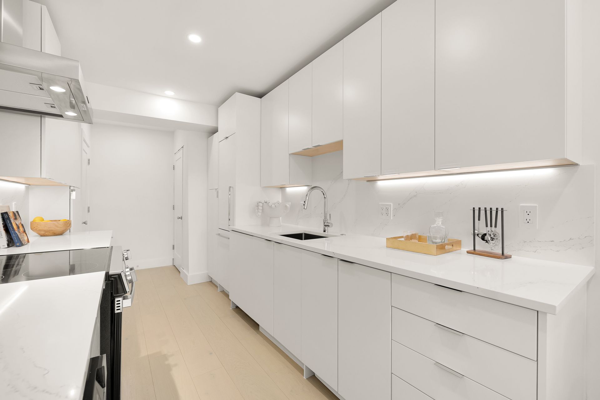White kitchen with white cabinets, stainless steel sink, and light-colored countertops.