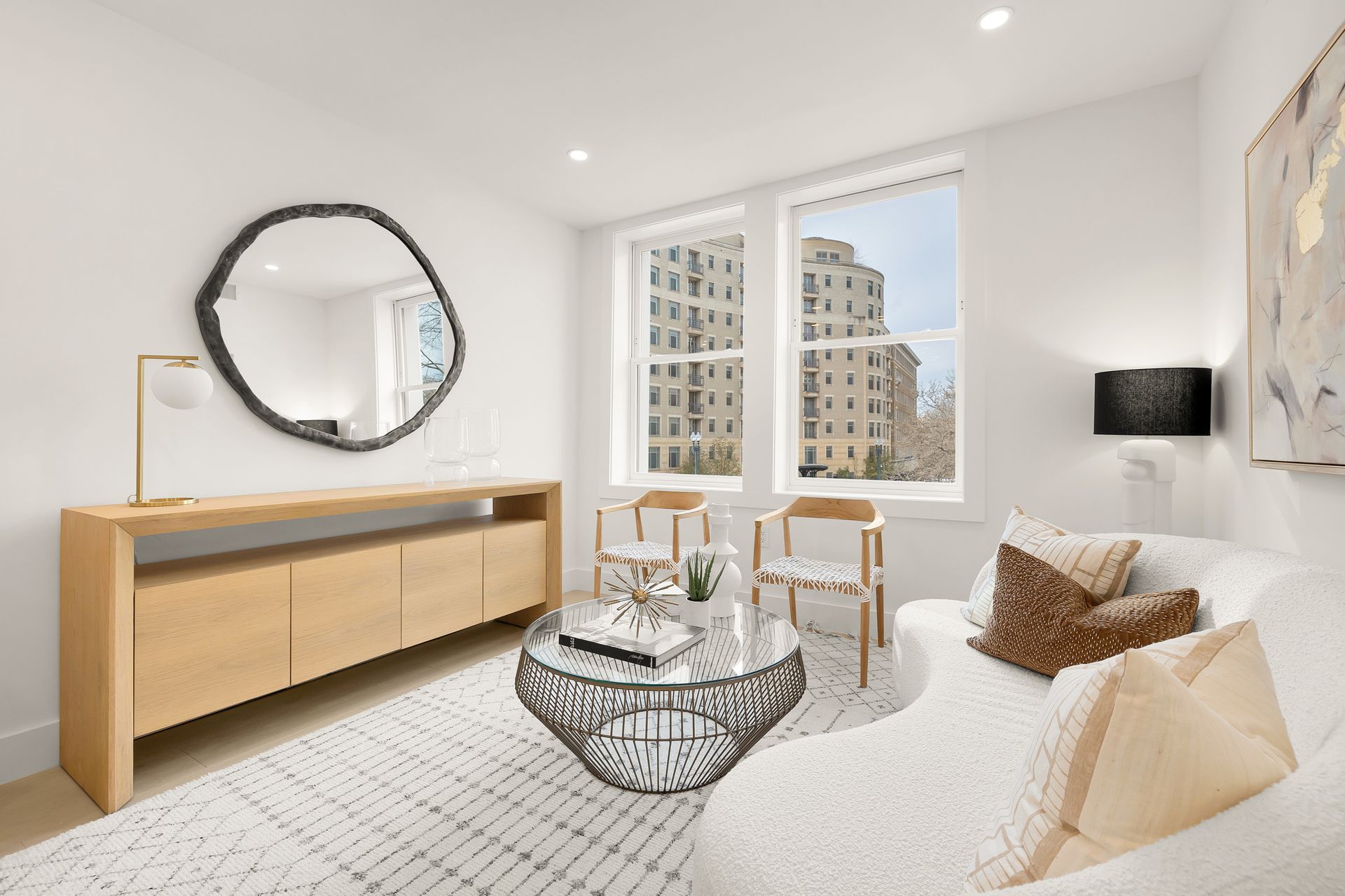 Bright living room with white walls, sofa, chairs, and large window overlooking an urban building.
