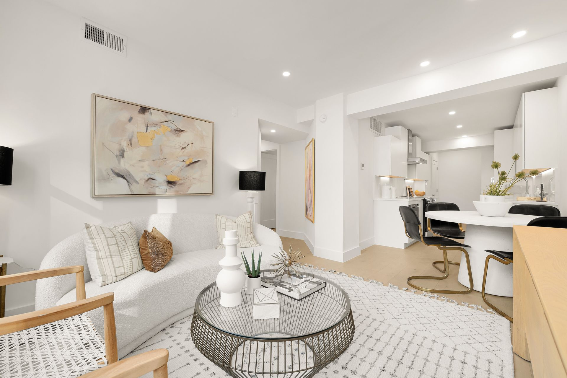 Living room with white walls, sofa, round coffee table, and open kitchen.