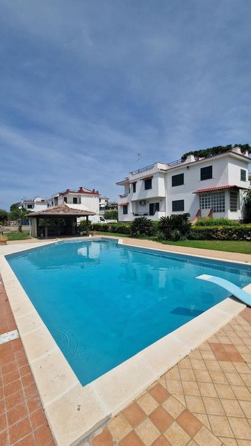 Piscina turchese del resort con ombrelloni bianchi, lettini e uno sfondo soleggiato sulla collina.