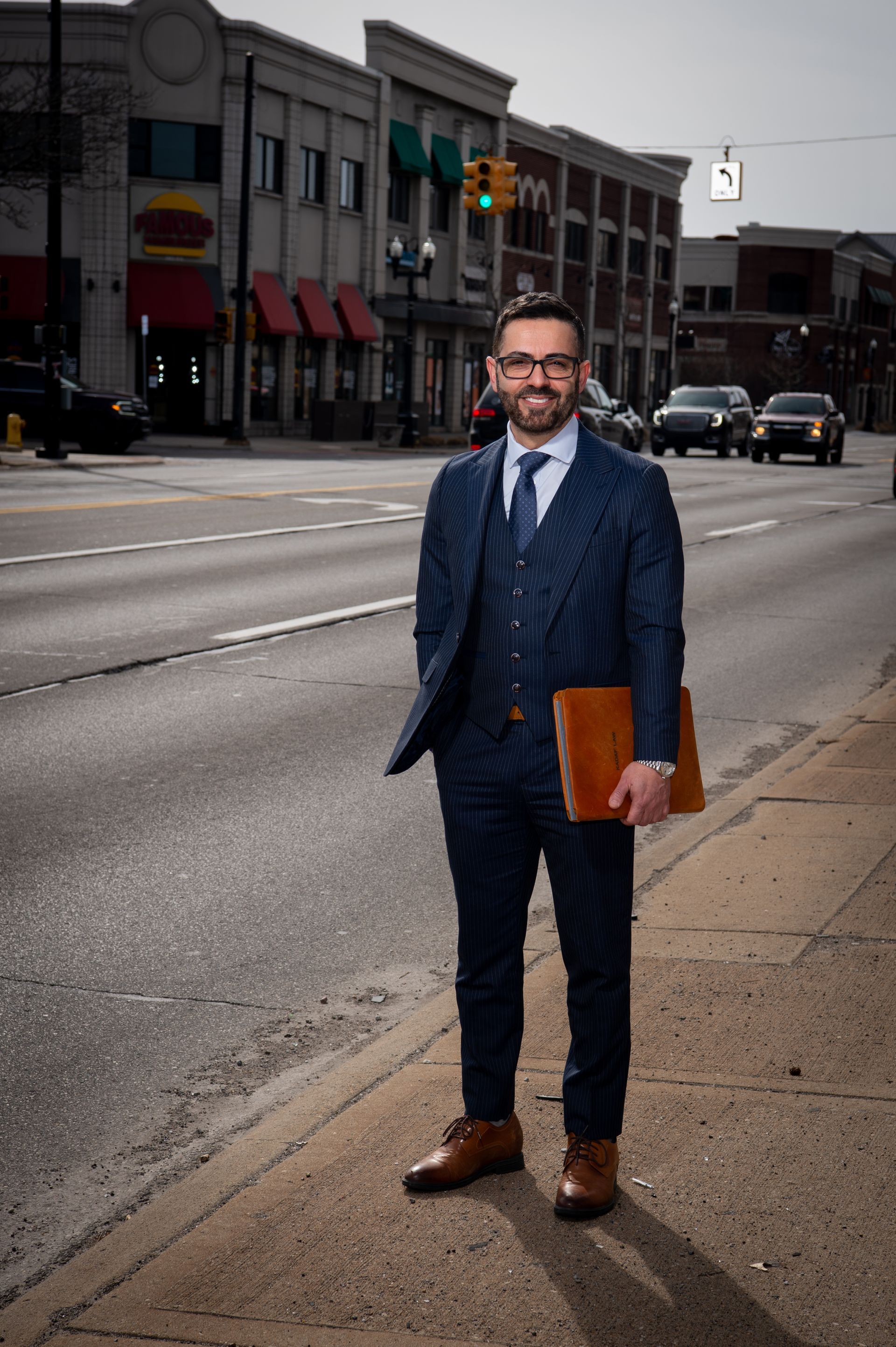 a man in a suit and tie is standing on the sidewalk holding a book .