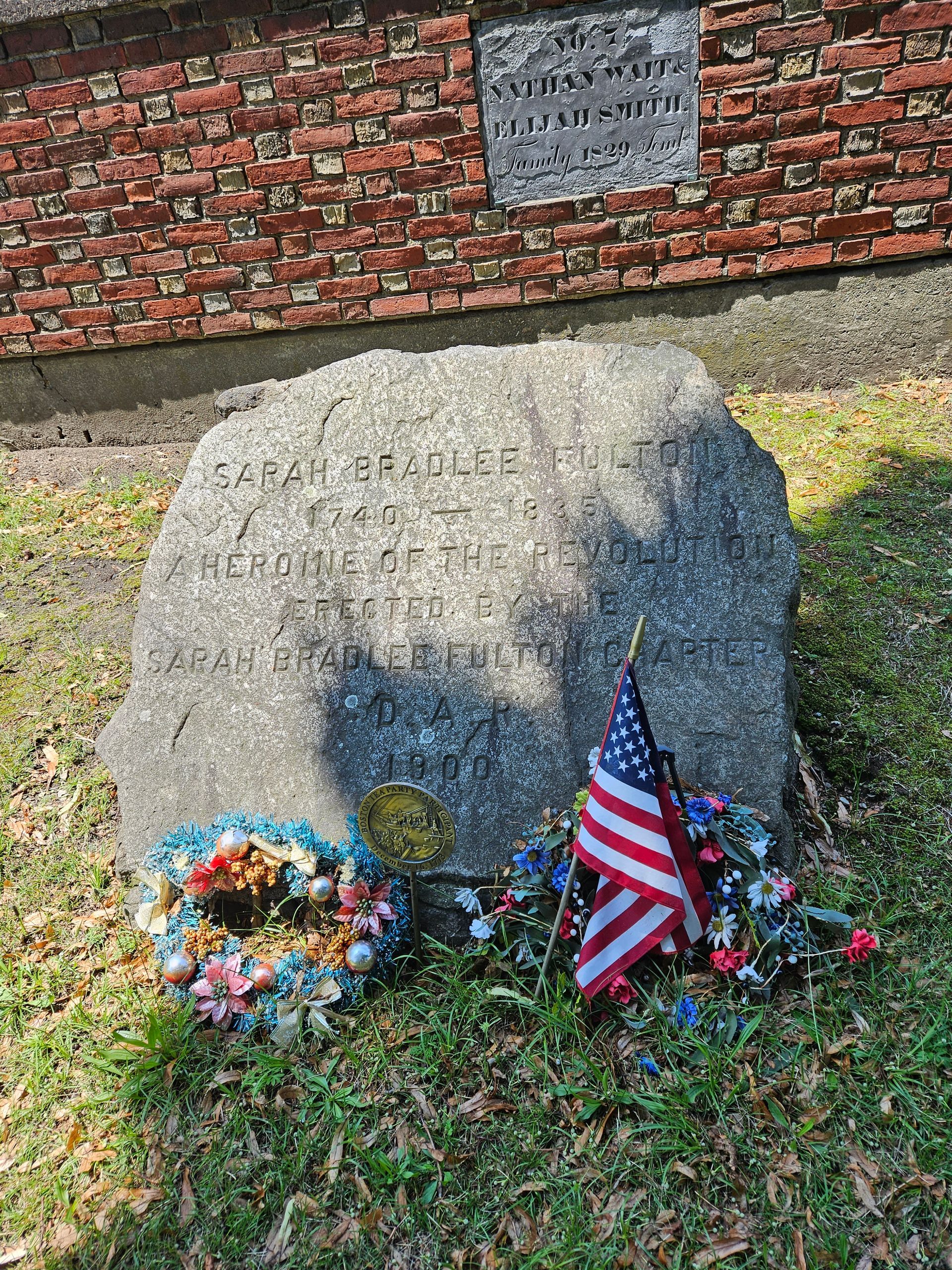 A large rock with a wreath and an american flag on it in front of a brick building.