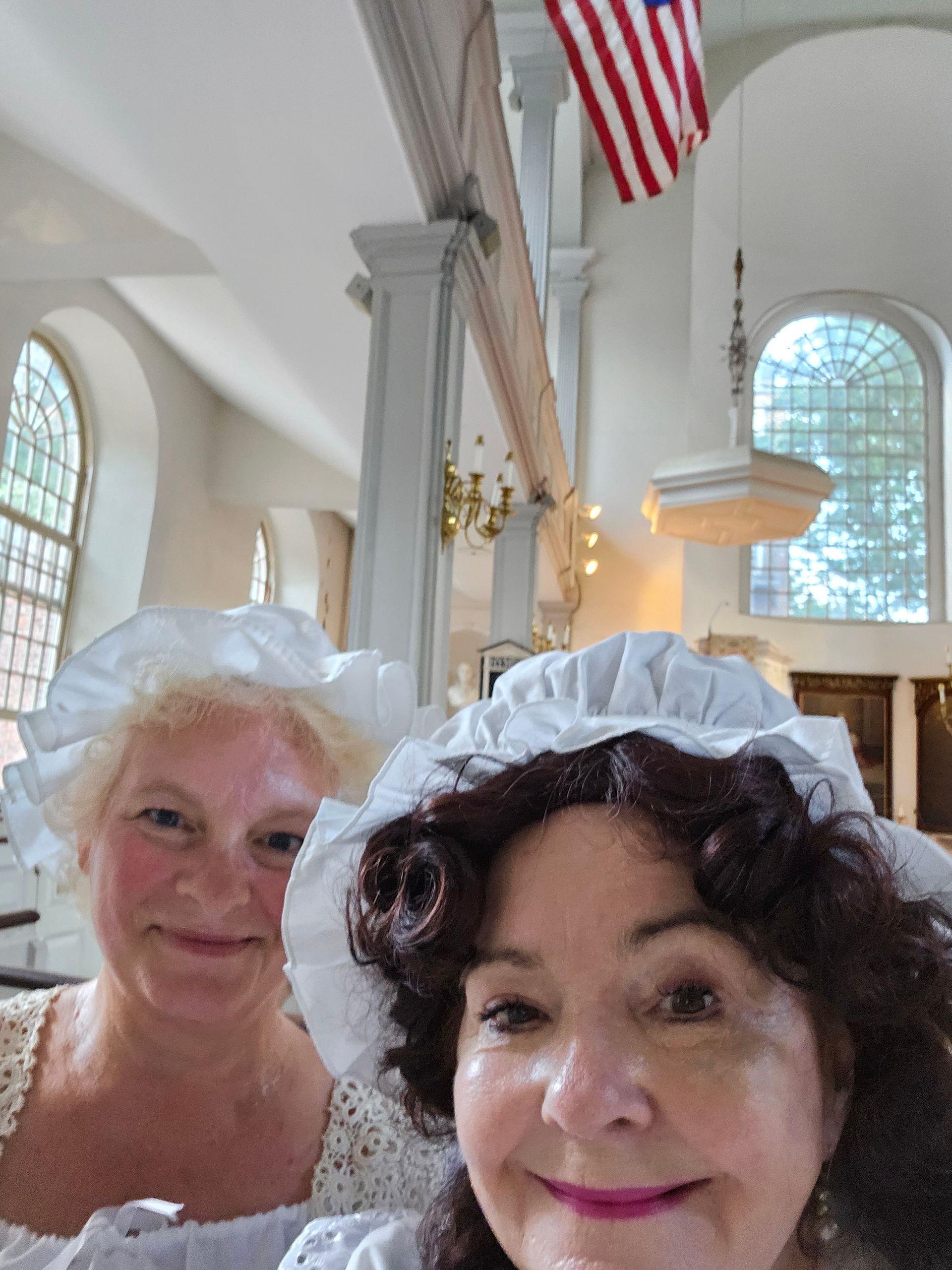 Two women are posing for a picture in a church with an american flag in the background
