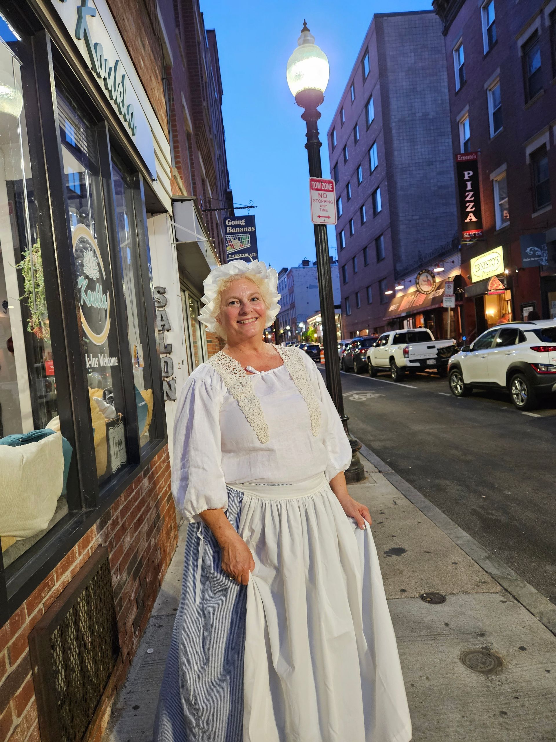 A woman in a white dress is standing on a sidewalk in front of a store.