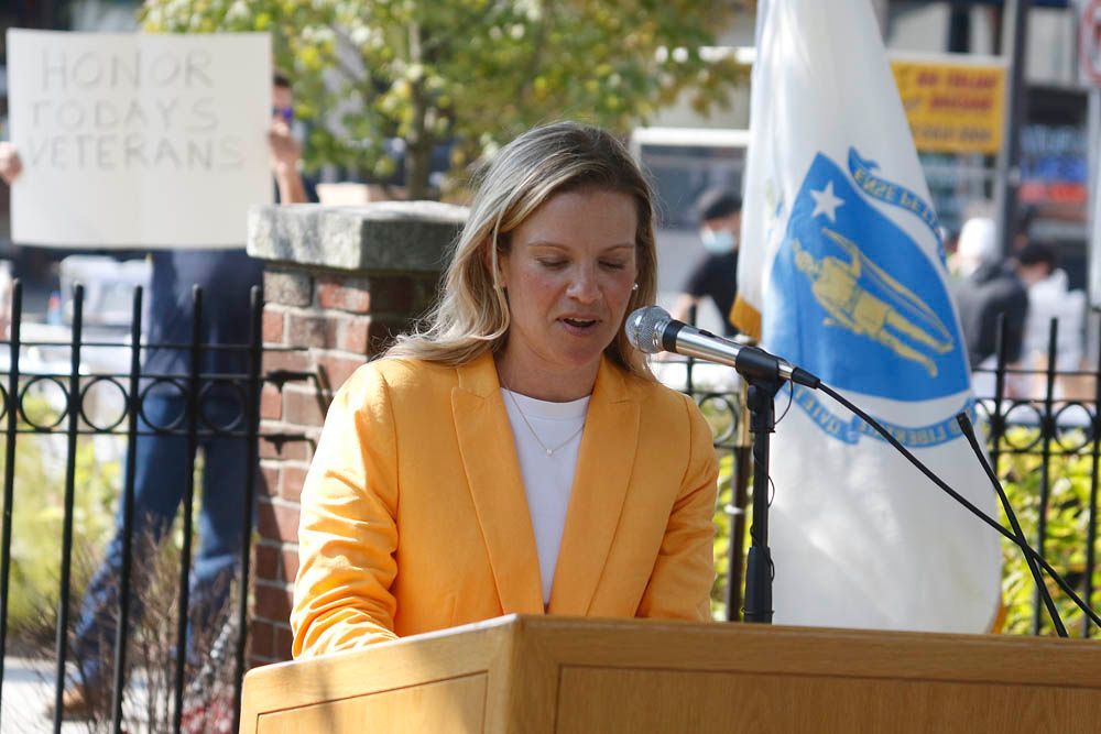 A woman in a yellow jacket is giving a speech at a podium