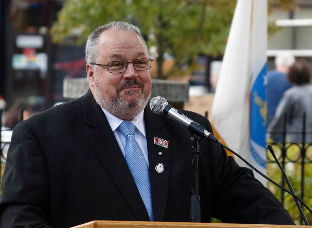 A man in a suit and tie is standing at a podium speaking into a microphone.