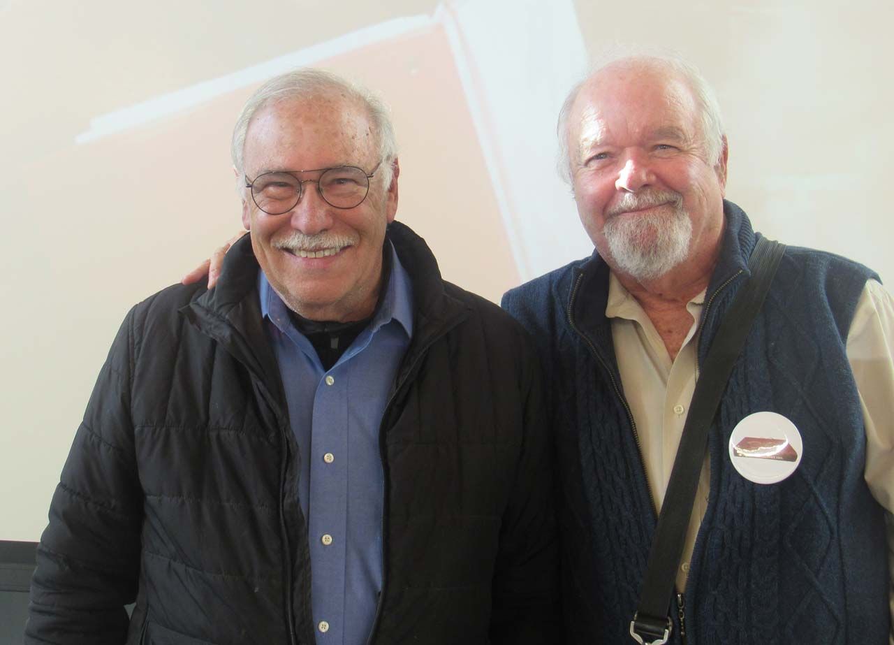 Two men are posing for a picture and one has a badge on his vest