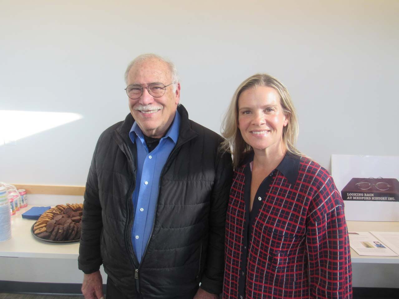A man and a woman are posing for a picture in front of a table with a cake on it.
