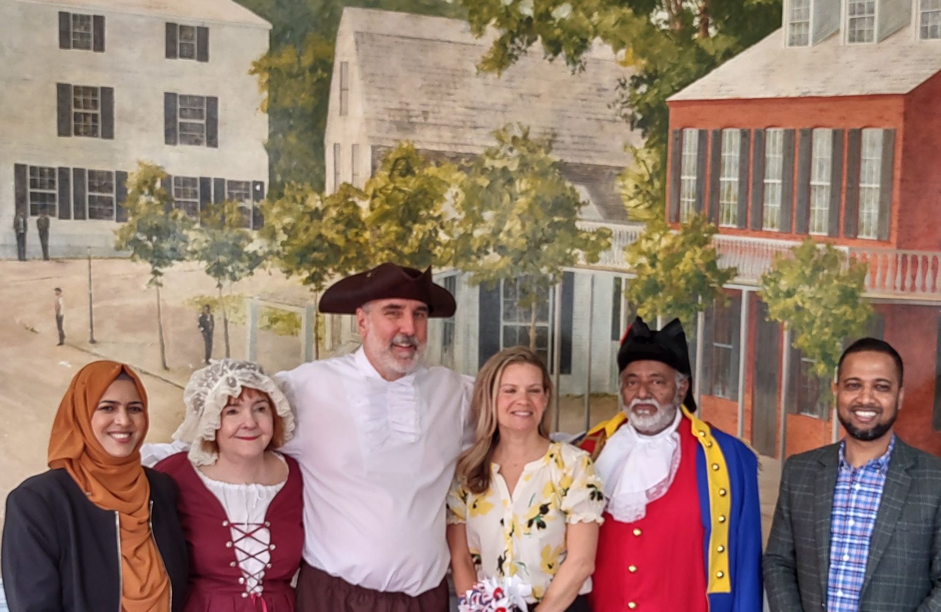 A group of people are posing for a picture in front of a painting.