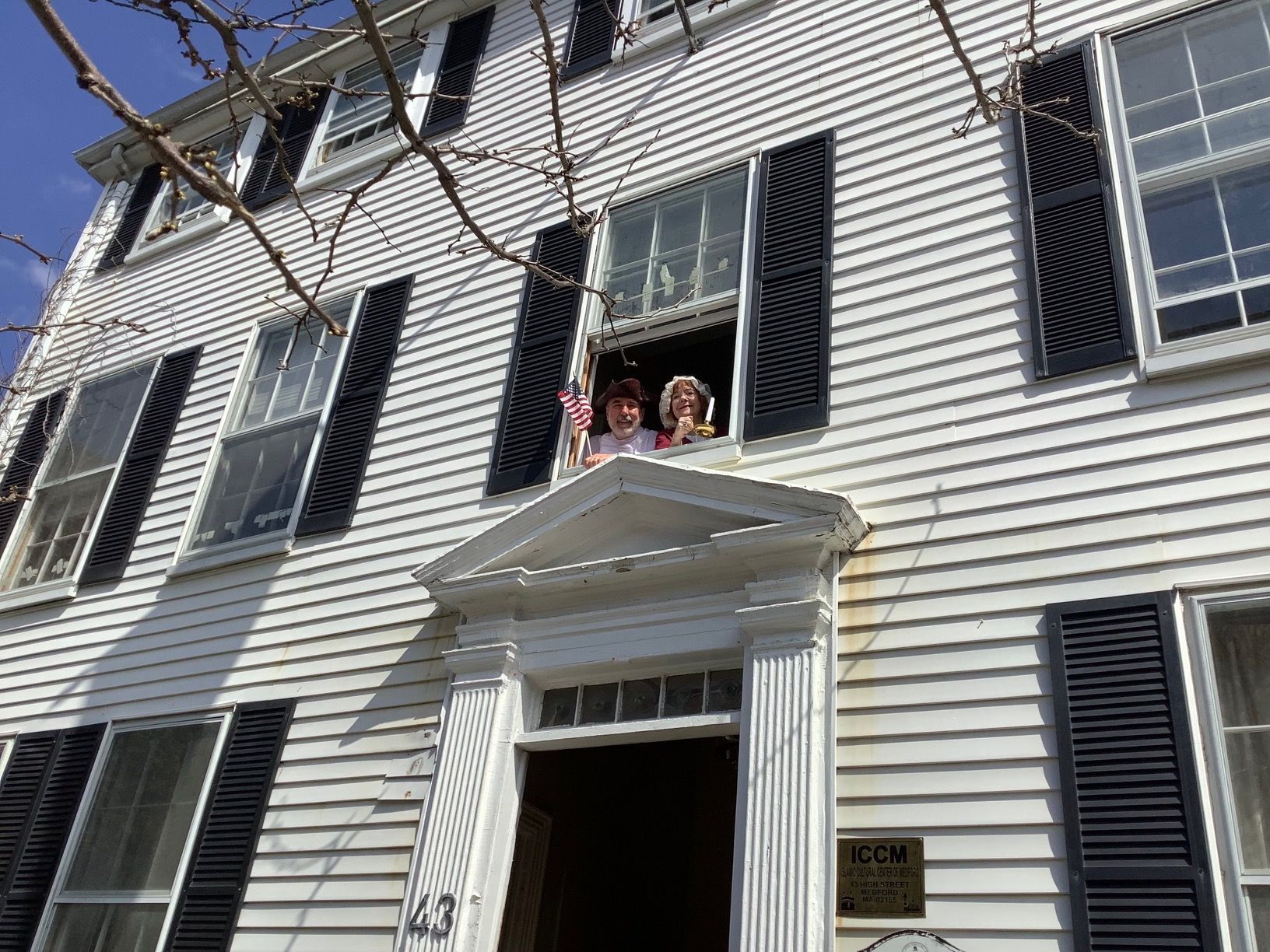 Two people are standing on the porch of a white house.