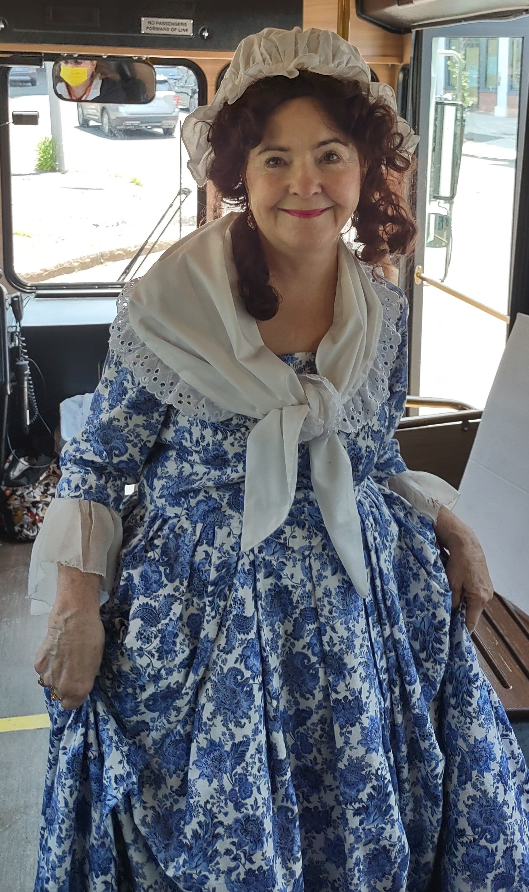 A woman in a blue and white dress is standing in front of a bus.