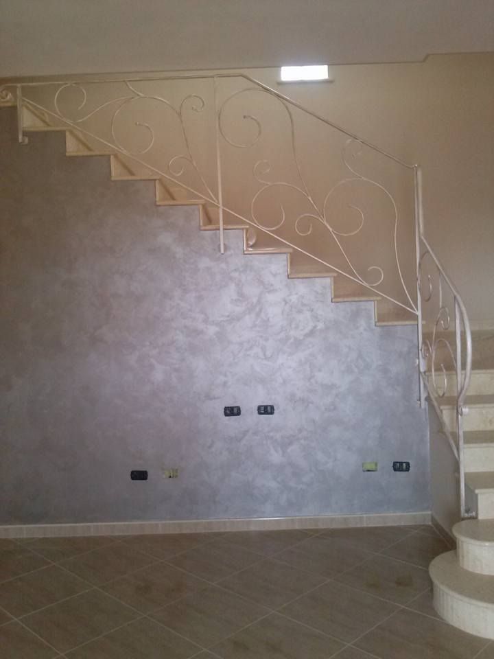 Una scala con ringhiera in ferro battuto si trova in una stanza vuota.