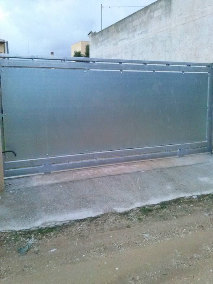 Un grande cancello di metallo si trova sul ciglio di una strada sterrata.