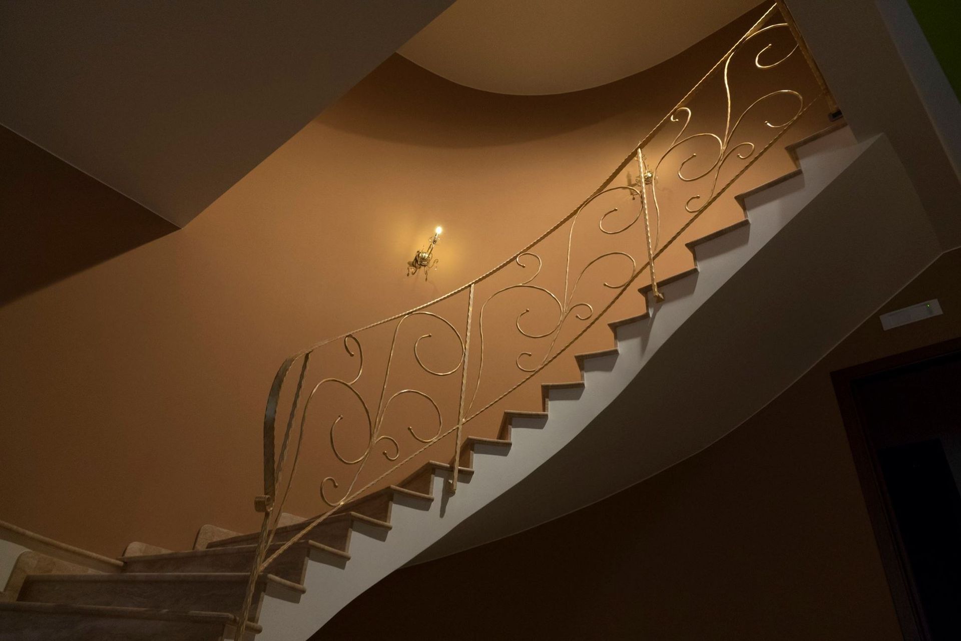 Una scala con una ringhiera dorata e una luce sul muro