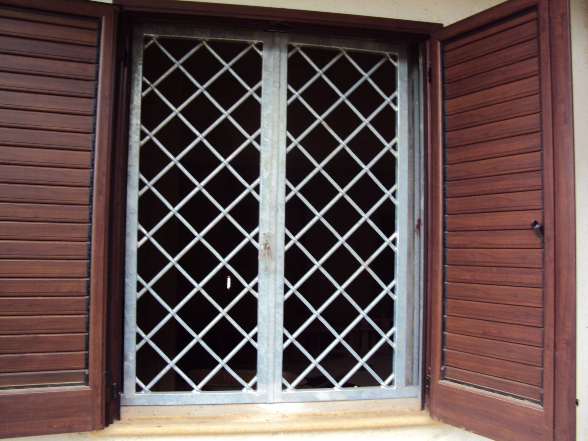 Una finestra con persiane in legno e una griglia metallica