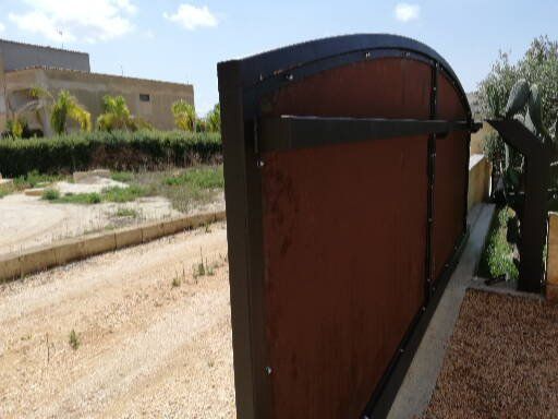 Una recinzione marrone con la sommità curva si trova accanto a una strada sterrata.