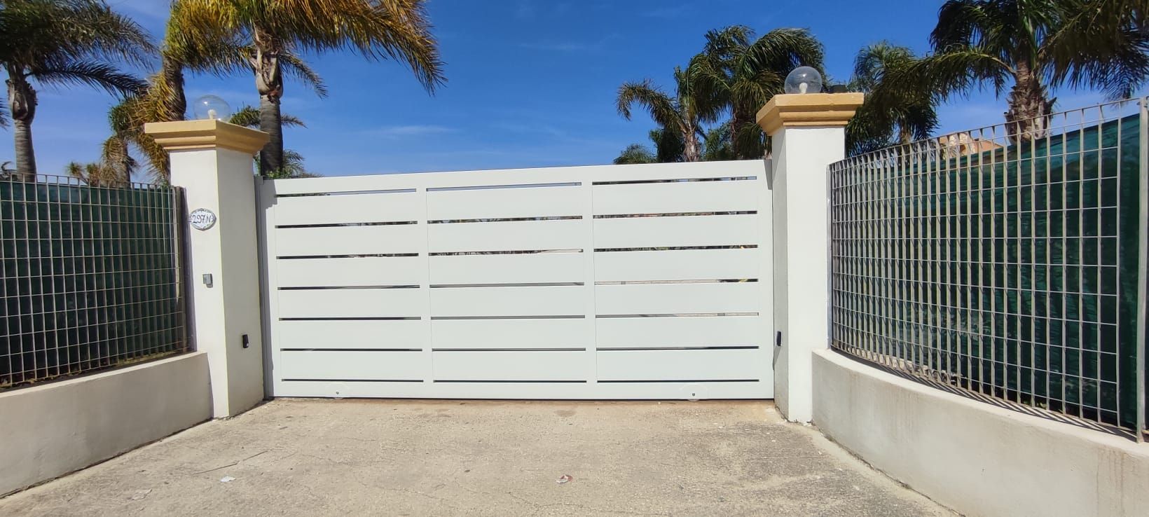 Un cancello bianco è aperto su un vialetto con palme sullo sfondo