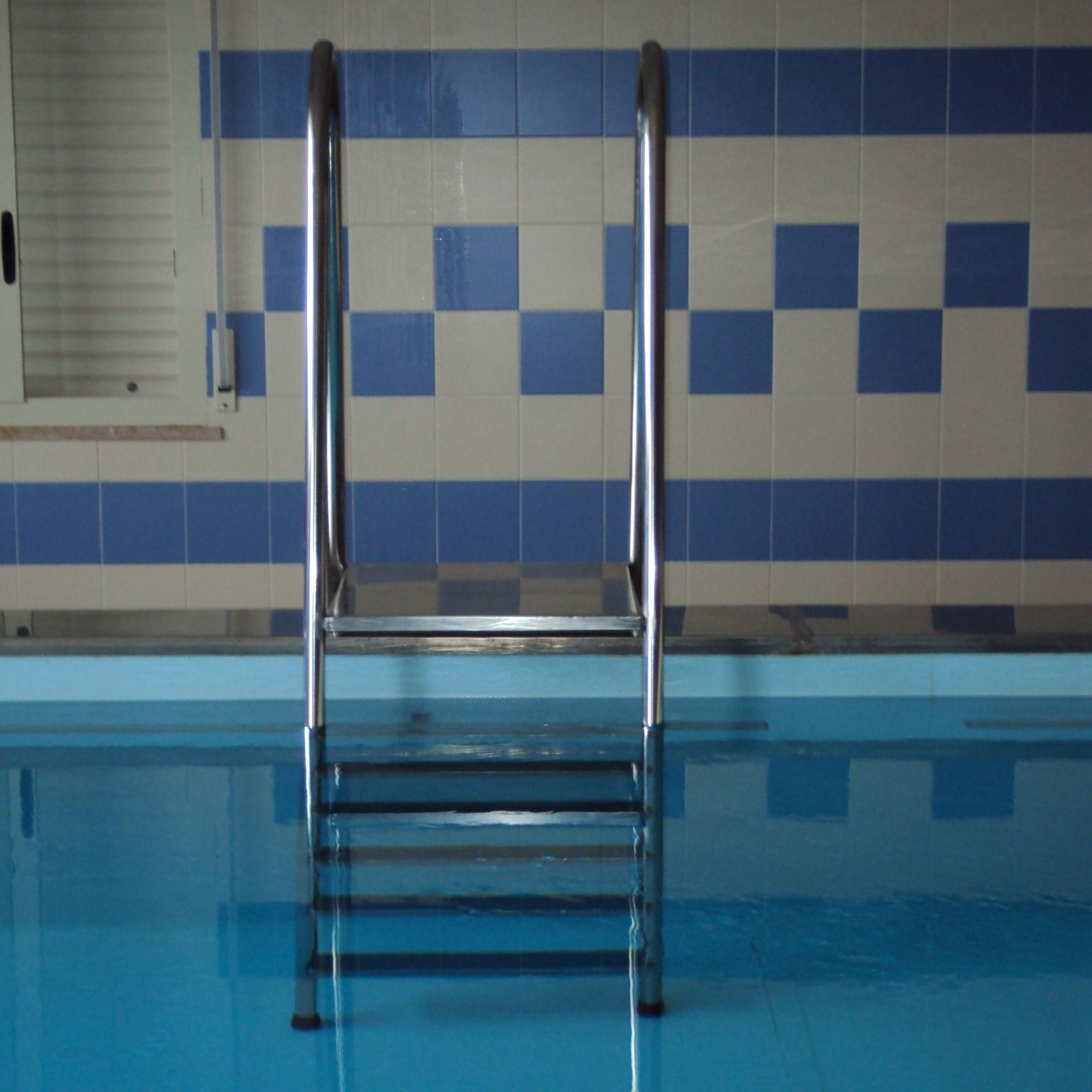 Una piscina con piastrelle blu e bianche e una scaletta
