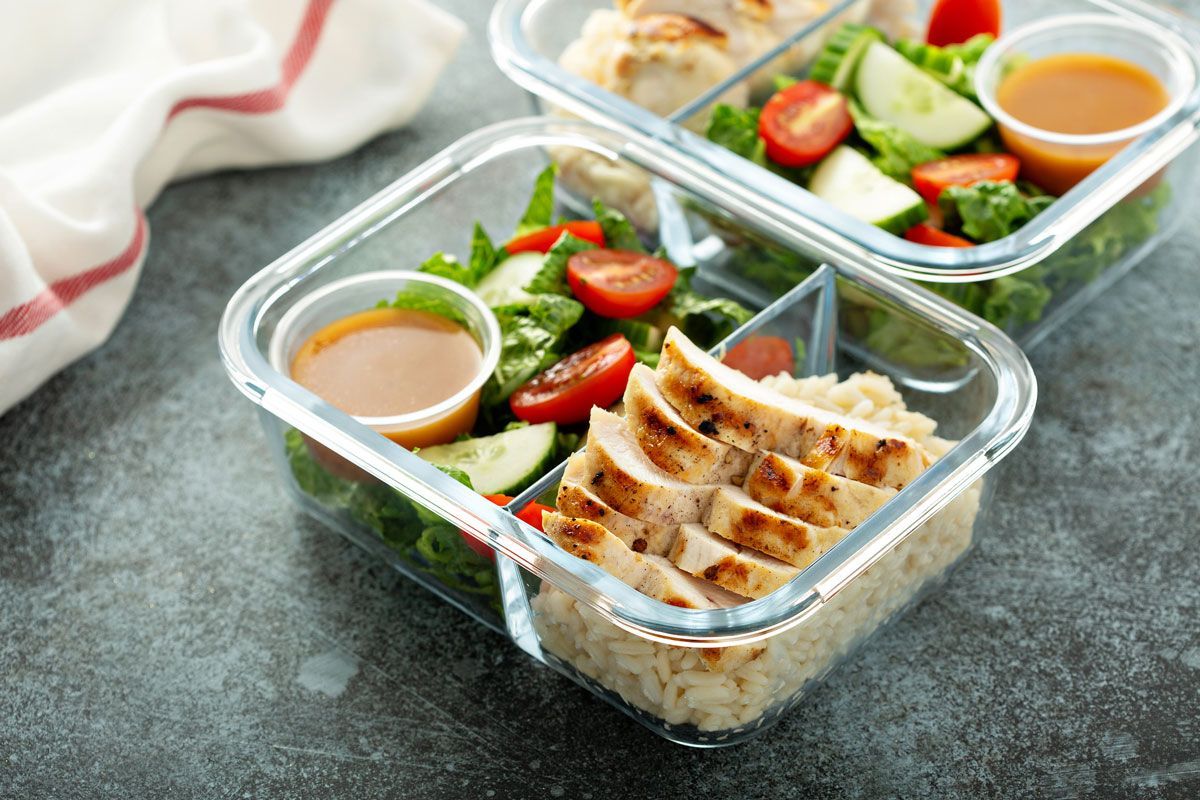 Two glass meal prep containers with grilled chicken, quinoa, salad, cherry tomatoes, and dressing.