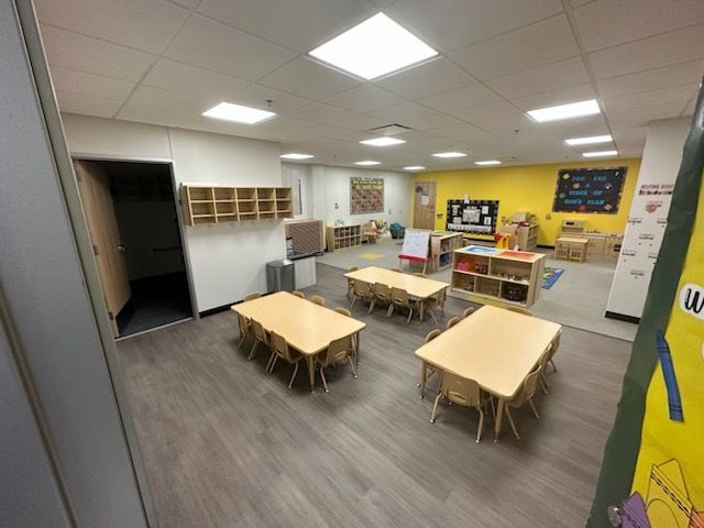 A classroom with tables and chairs and a yellow wall.