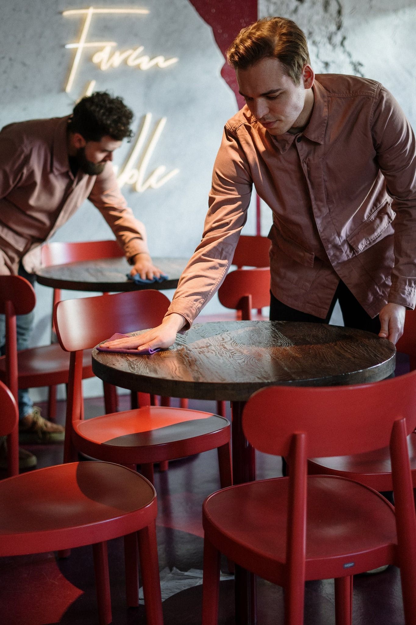 Two men are cleaning tables and chairs in a restaurant.