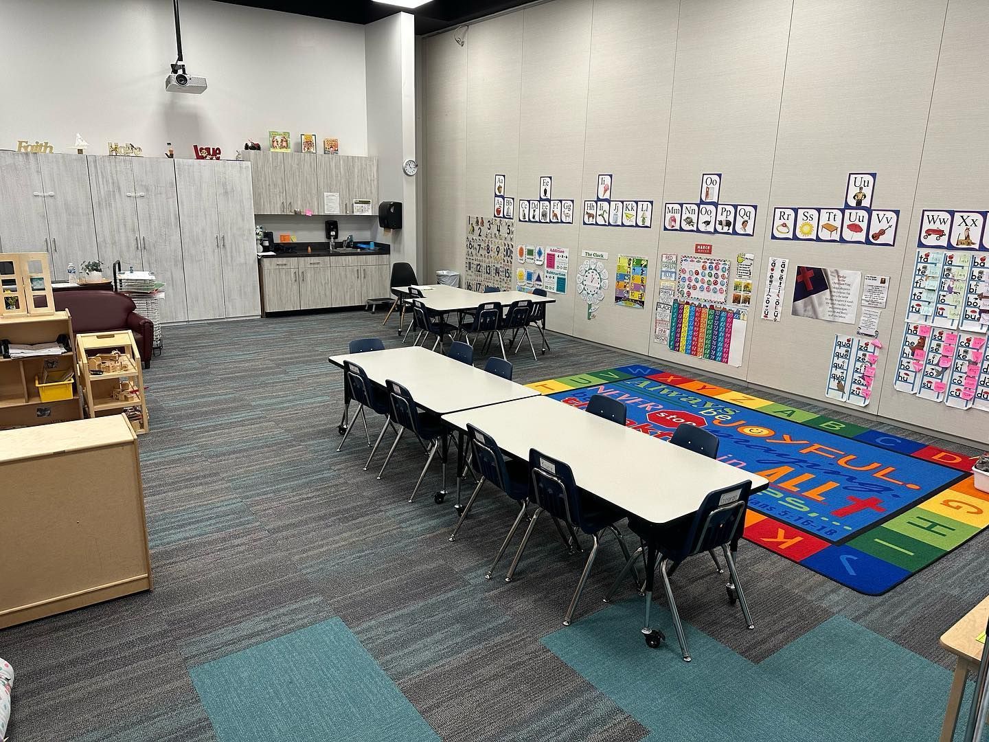 A classroom with tables and chairs and a rug on the floor.