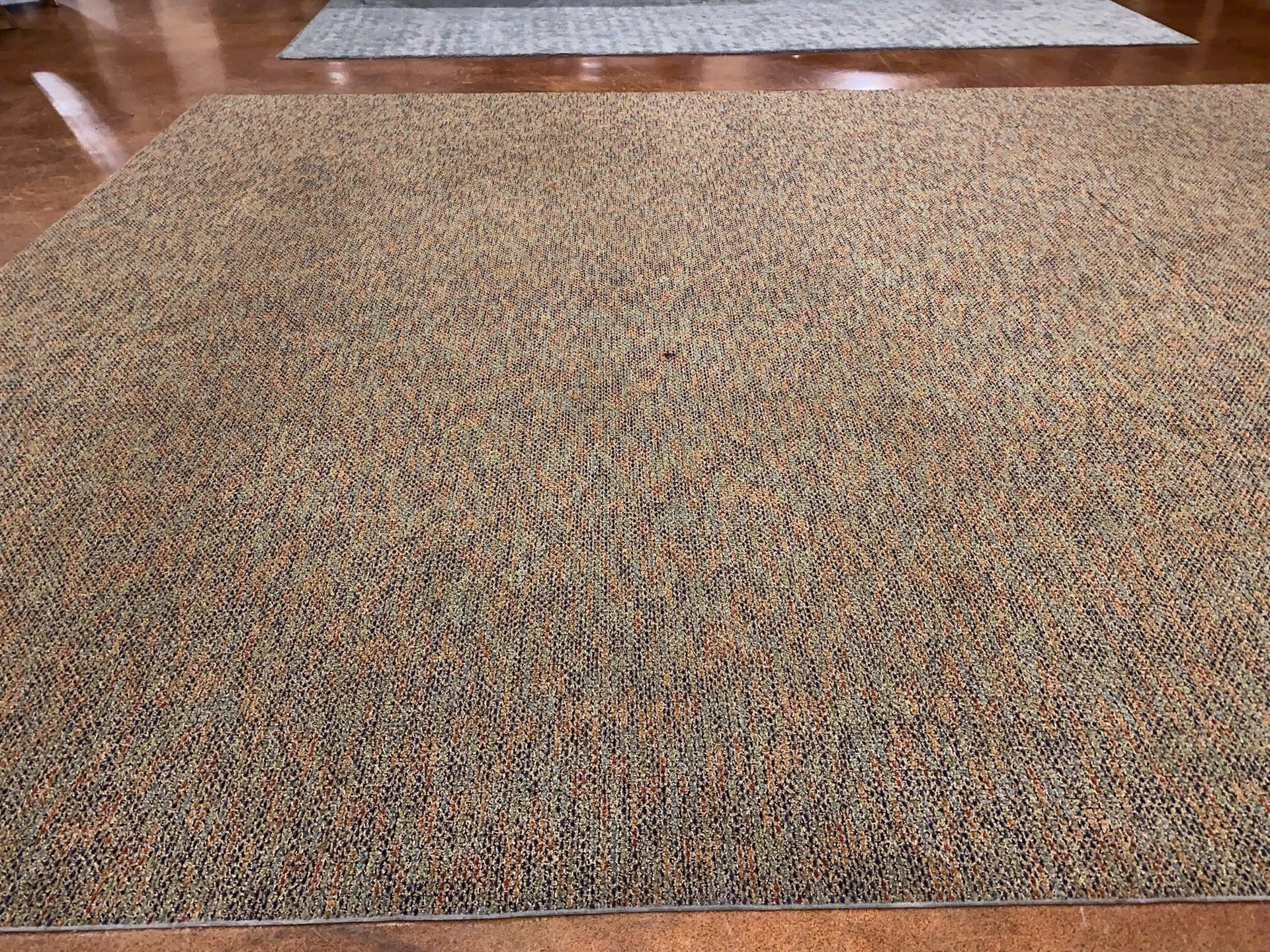 A large rug is sitting on a wooden floor in a living room.