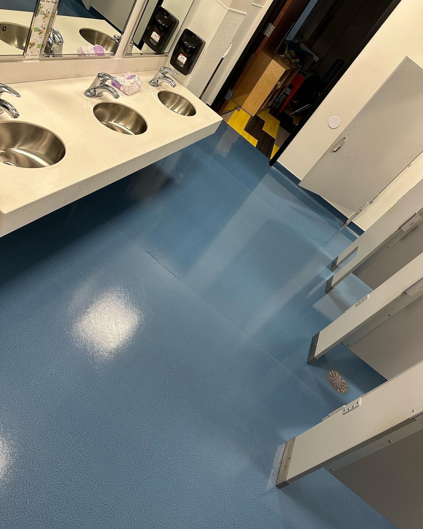 A bathroom with blue floors , sinks and toilets.
