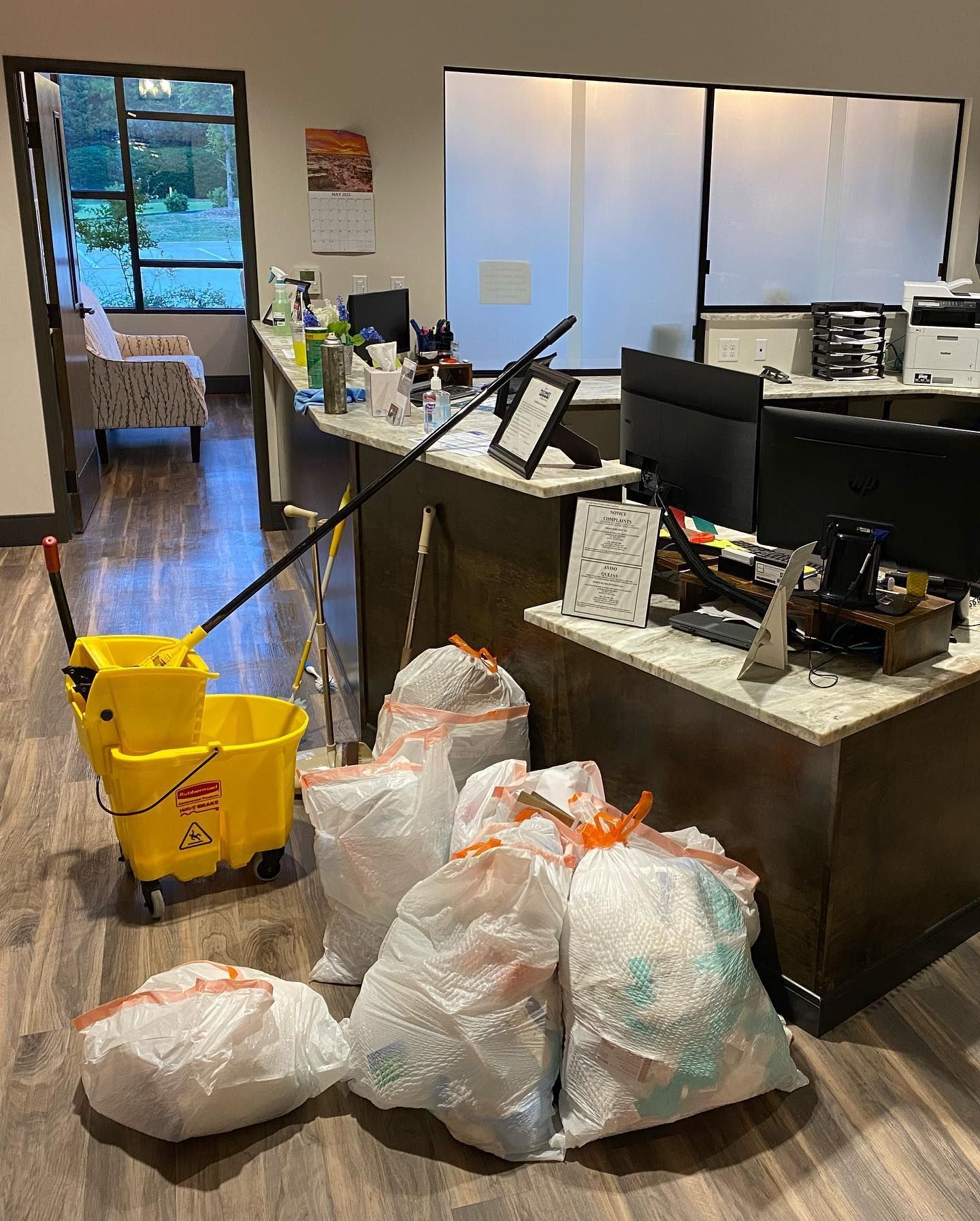 A yellow mop bucket is sitting next to a pile of trash bags in an office.