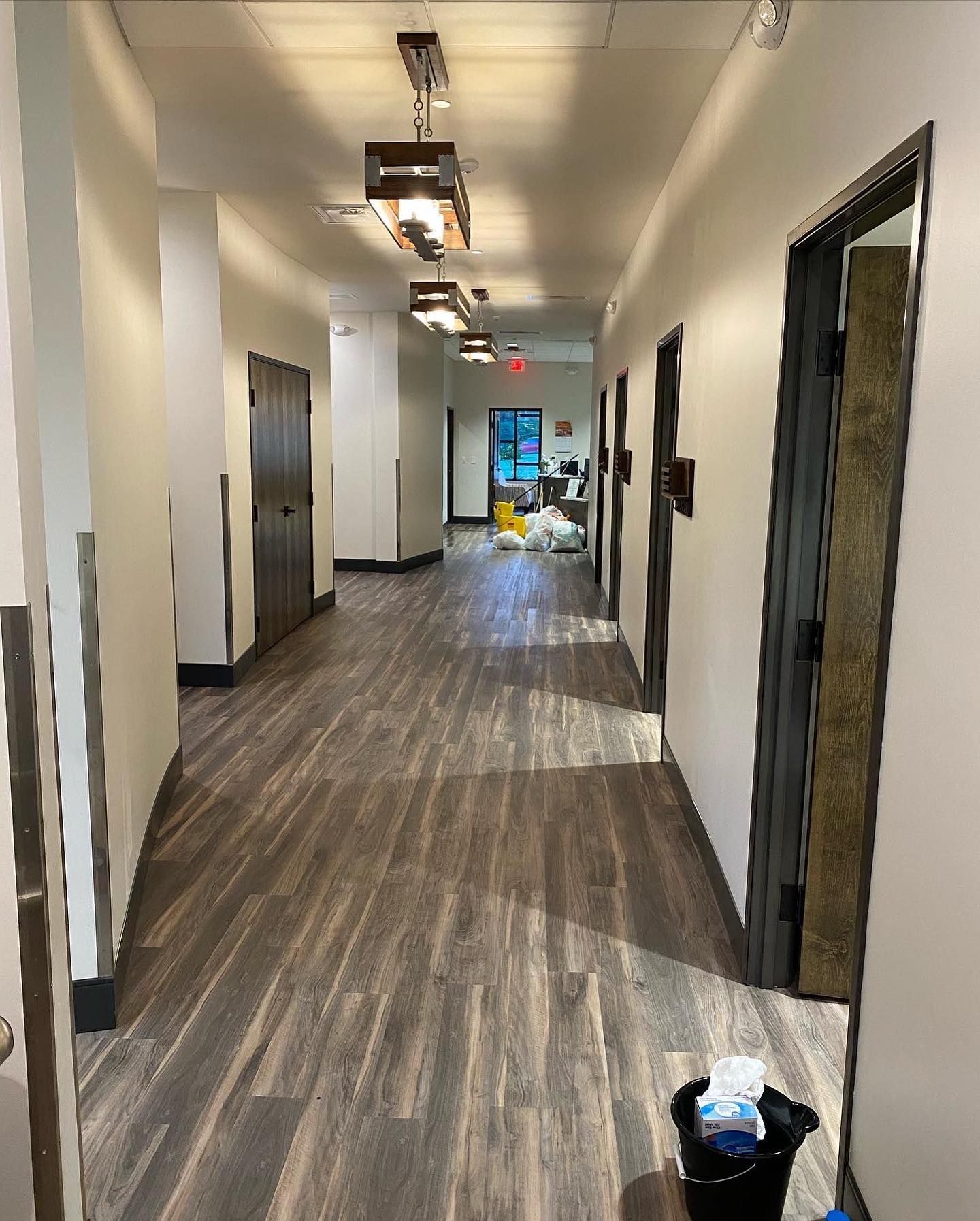 A long hallway with wooden floors and a bucket of tissues on the floor.