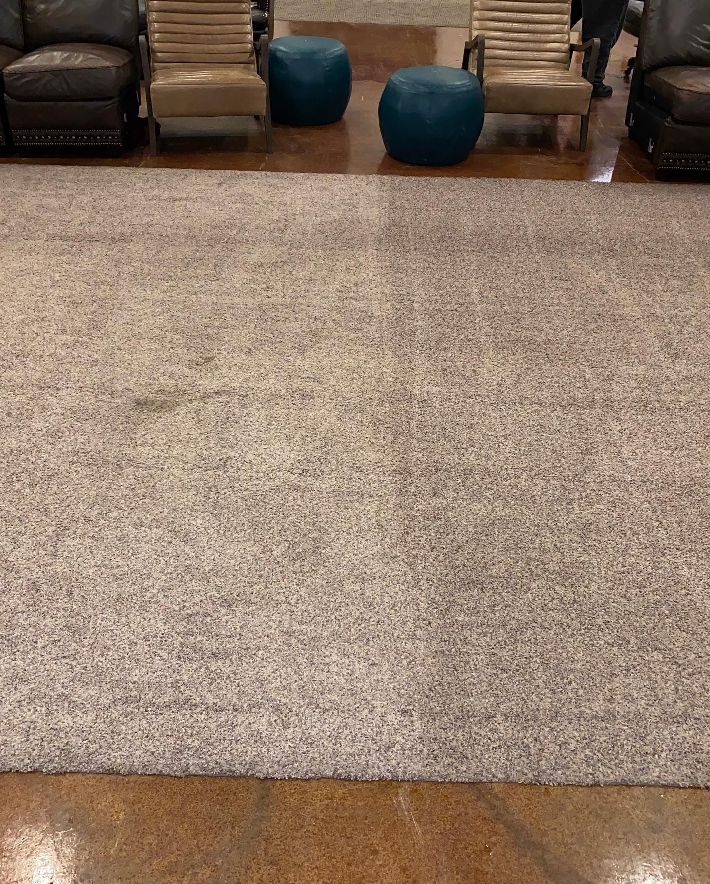 A large rug is sitting on the floor in a room with chairs and ottomans.