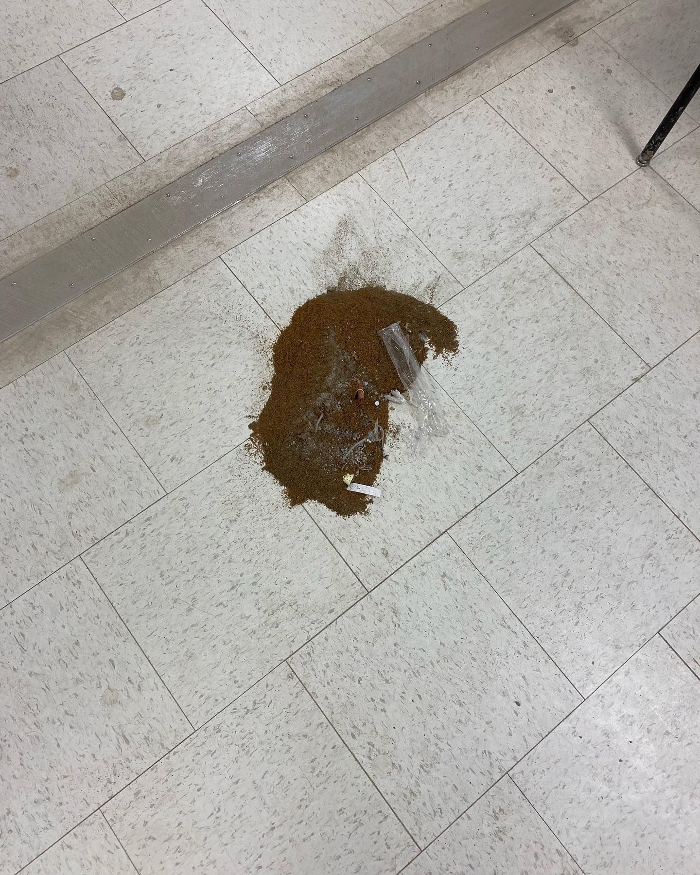 A pile of brown powder is sitting on a tiled floor.