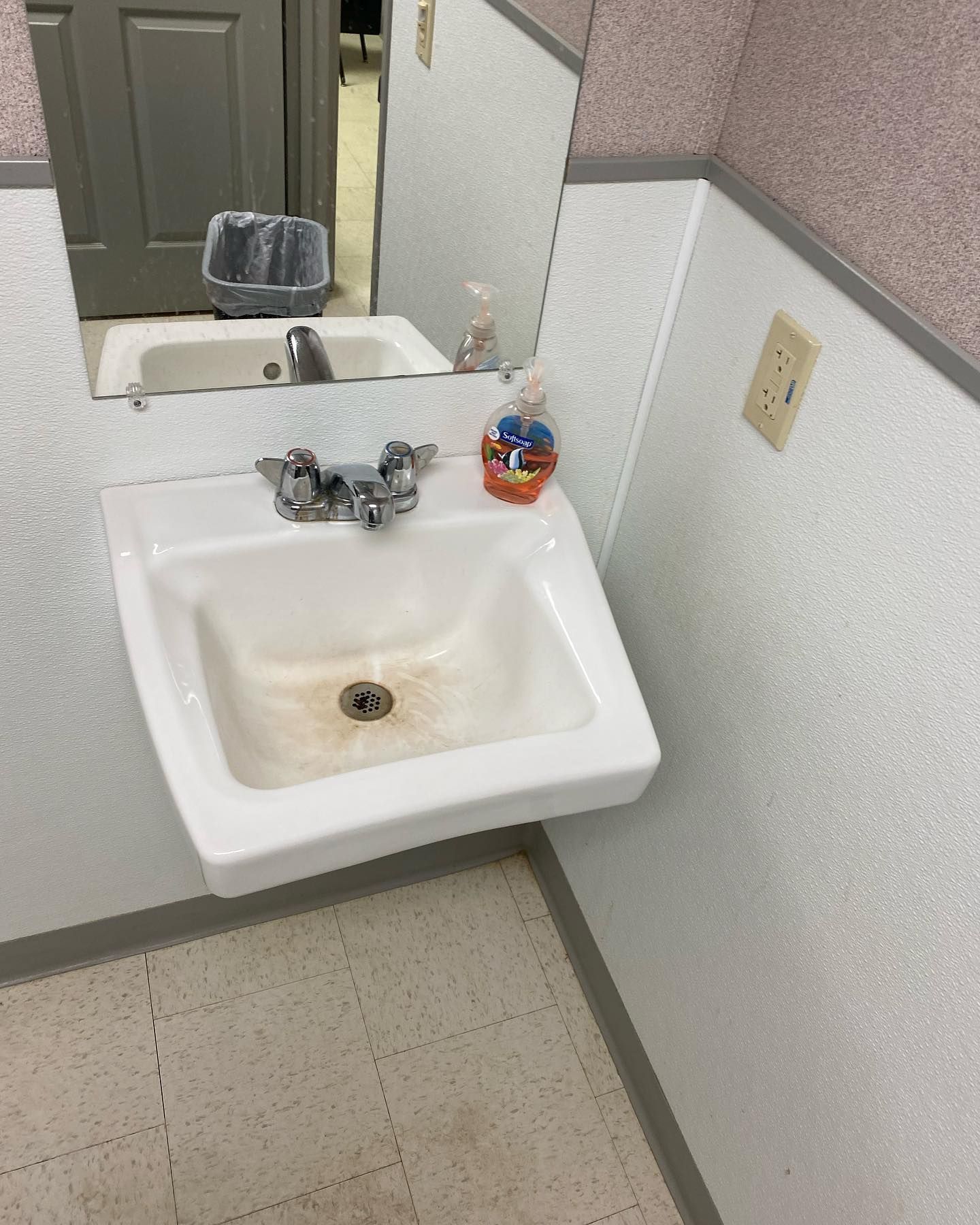 A bathroom sink with a soap dispenser and a mirror.