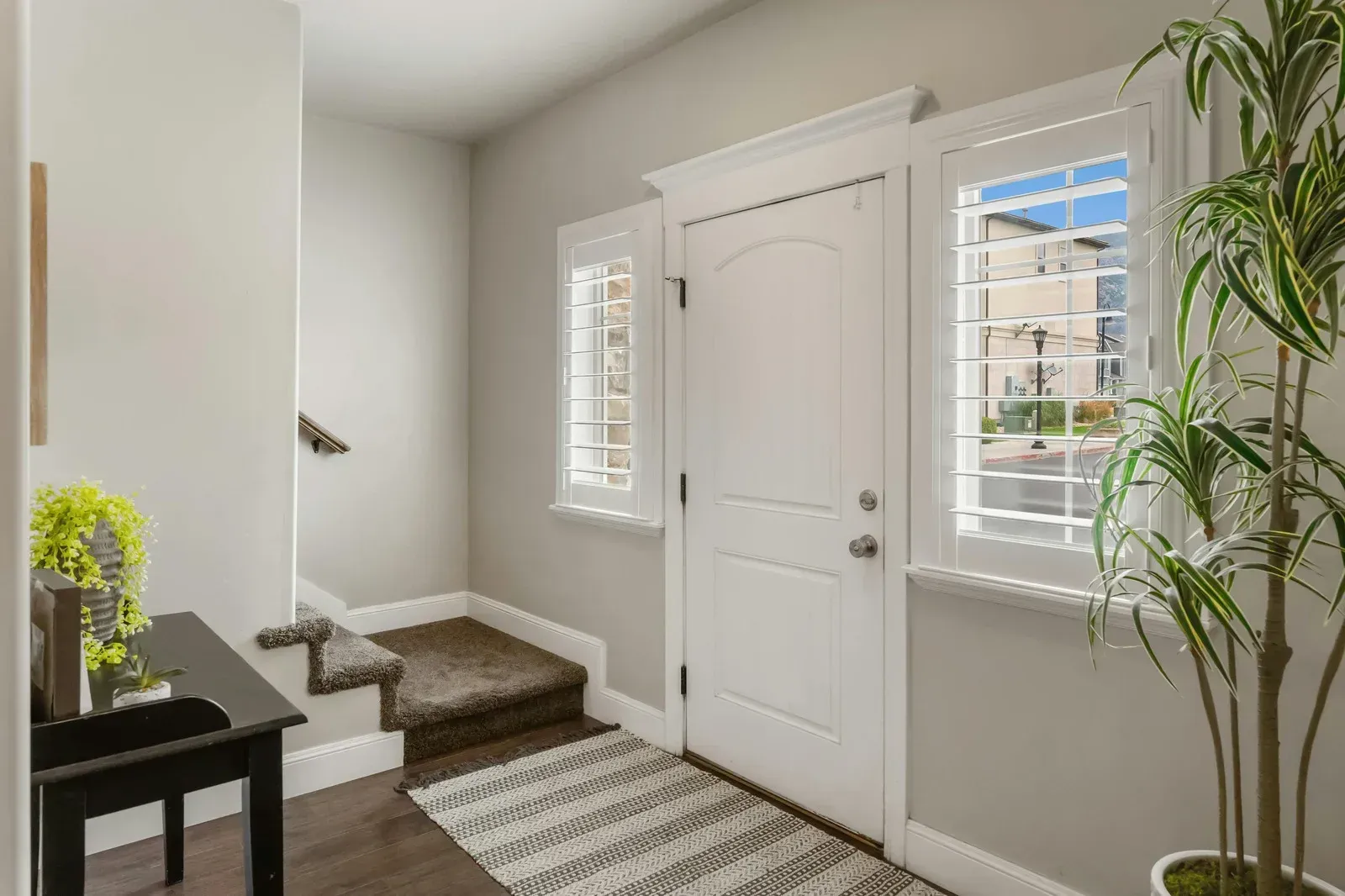 A hallway with a white door , stairs , a table and a potted plant.