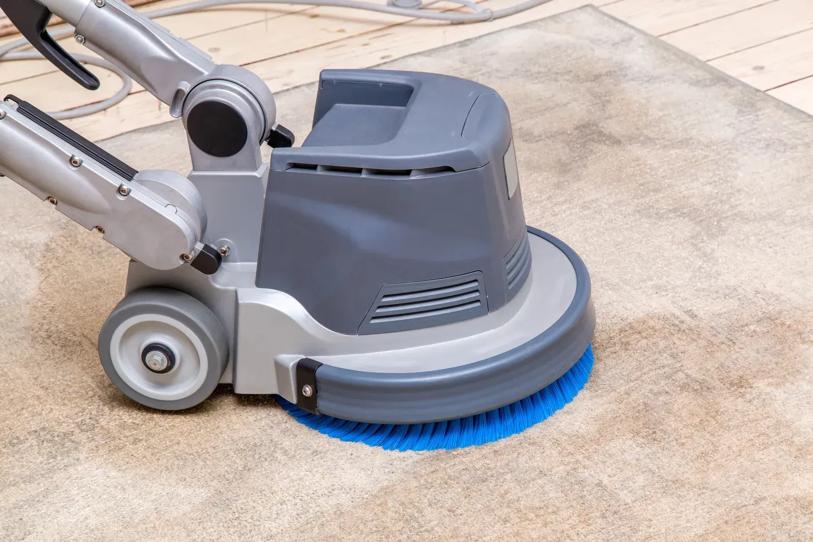 A machine is cleaning a carpet on a wooden floor.