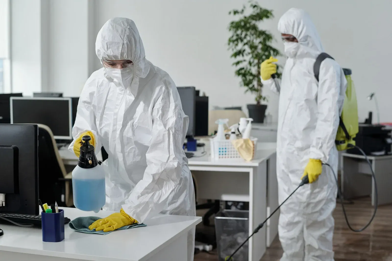 Two people in protective suits are cleaning an office.