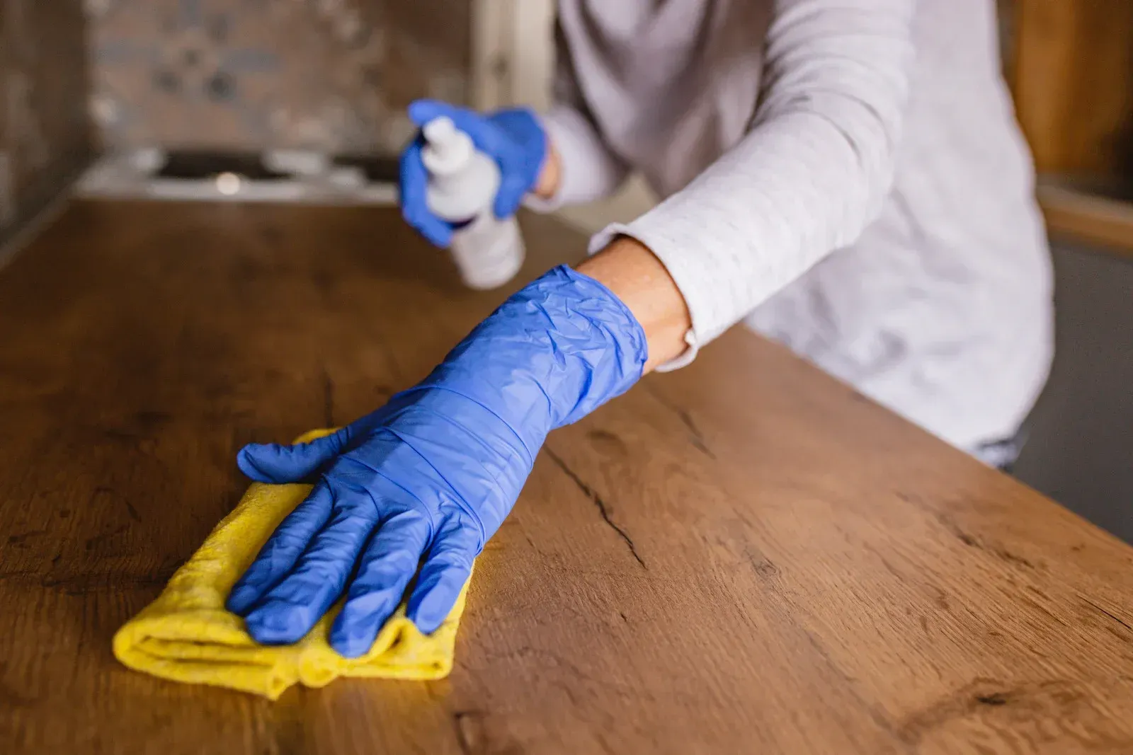 A person wearing blue gloves is cleaning a wooden table with a cloth.