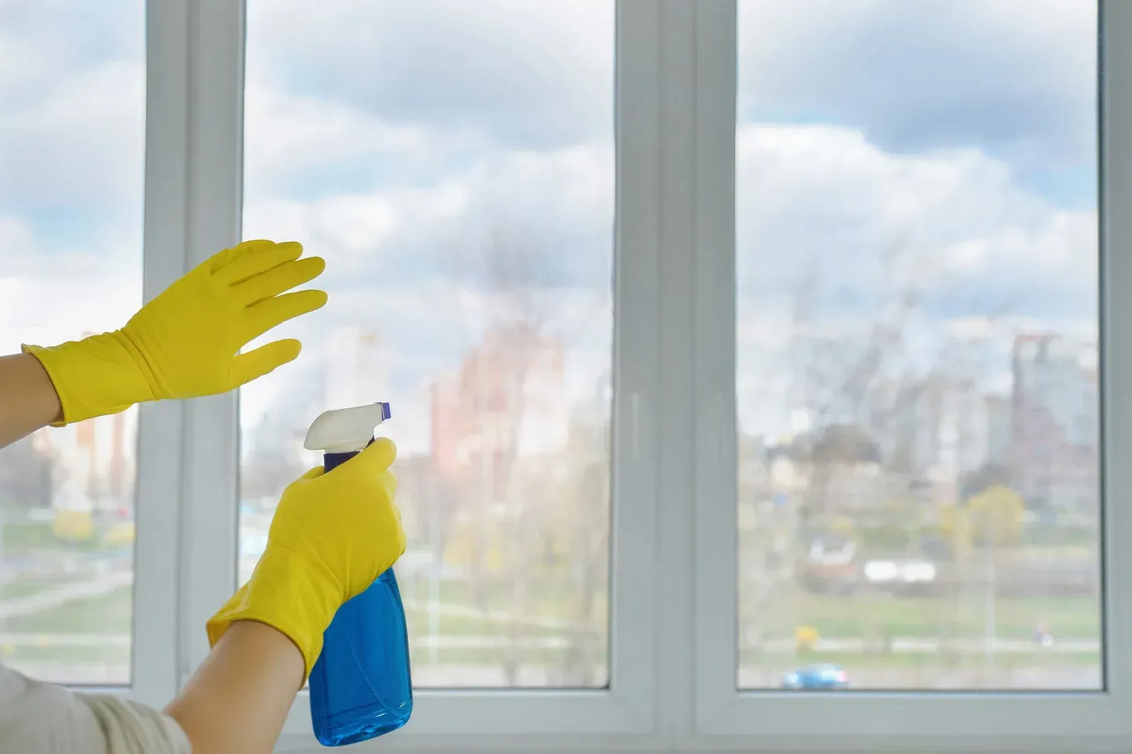 A person wearing yellow gloves is cleaning a window with a spray bottle.