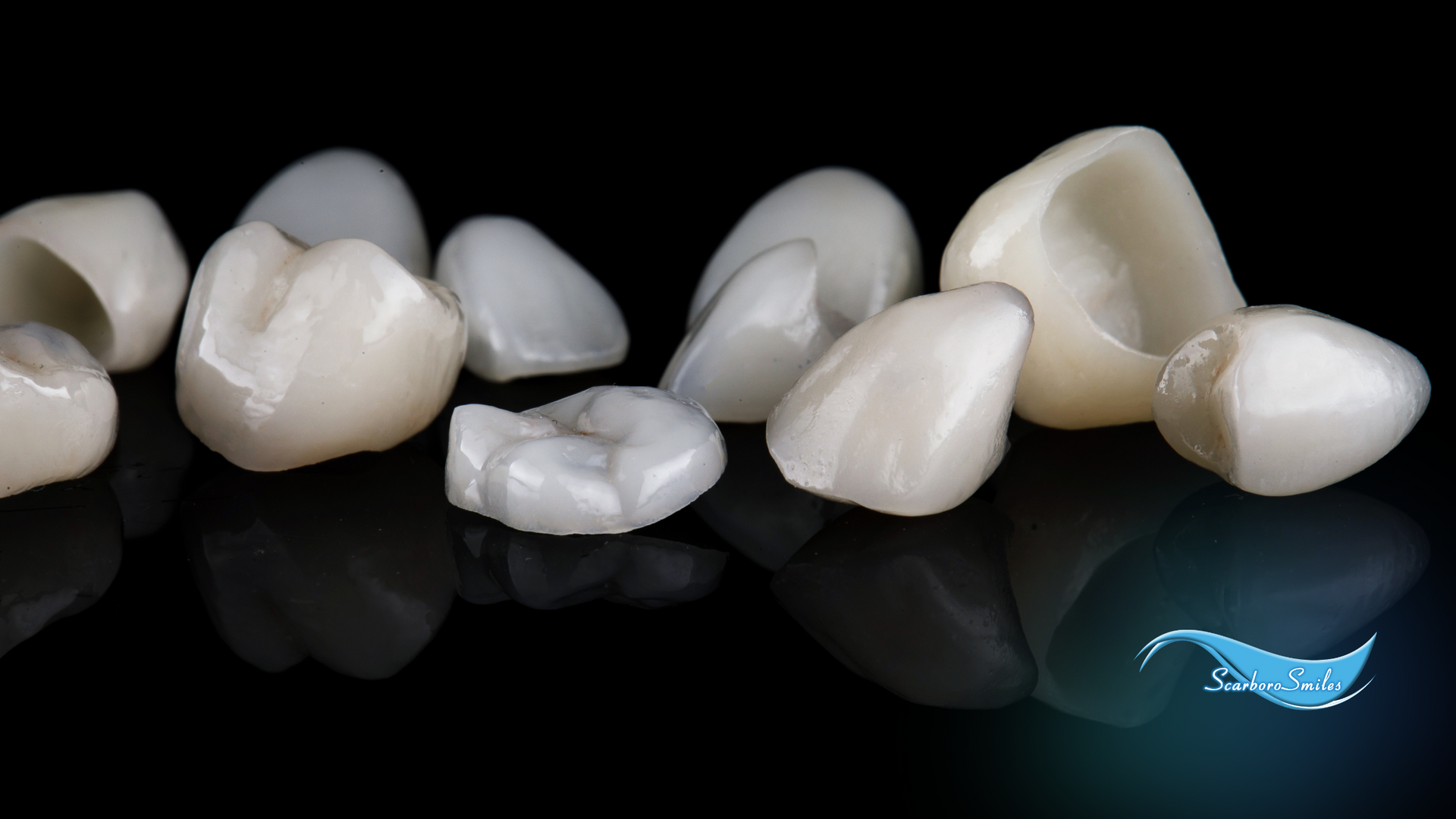 A group of dental crowns are lined up on a black surface.