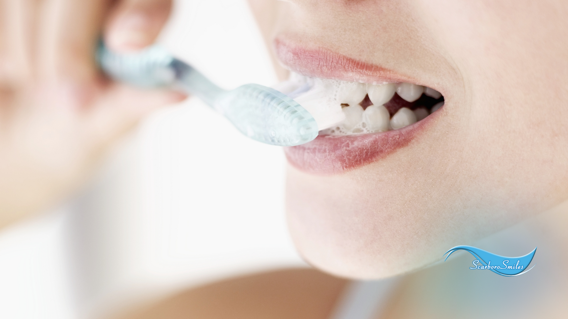 A woman is brushing her teeth with a blue toothbrush.