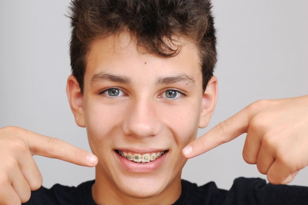 A young boy with braces is pointing at his teeth.