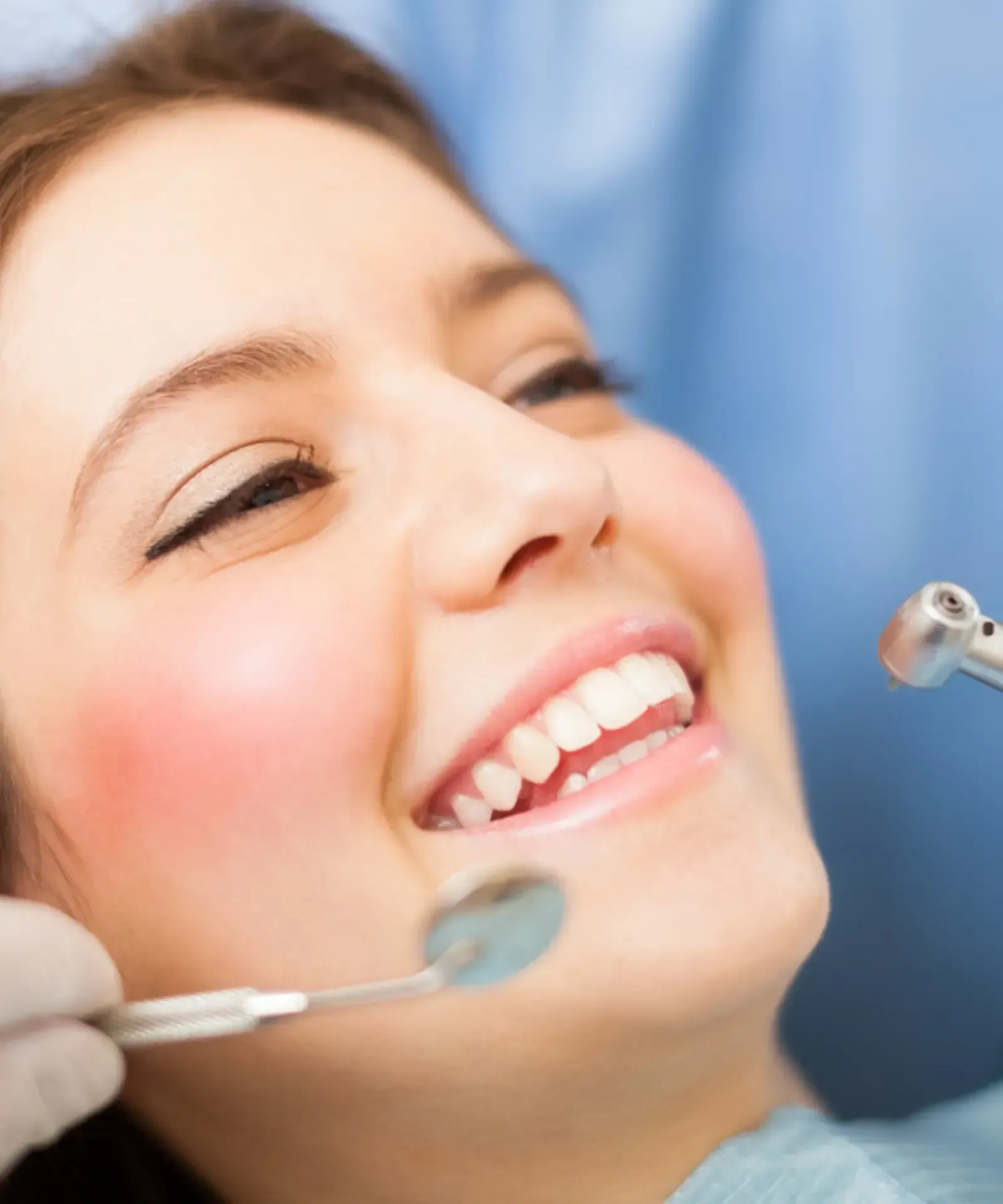 Woman with dark hair smiling, wearing teal scrubs, set against a wood-paneled wall.
